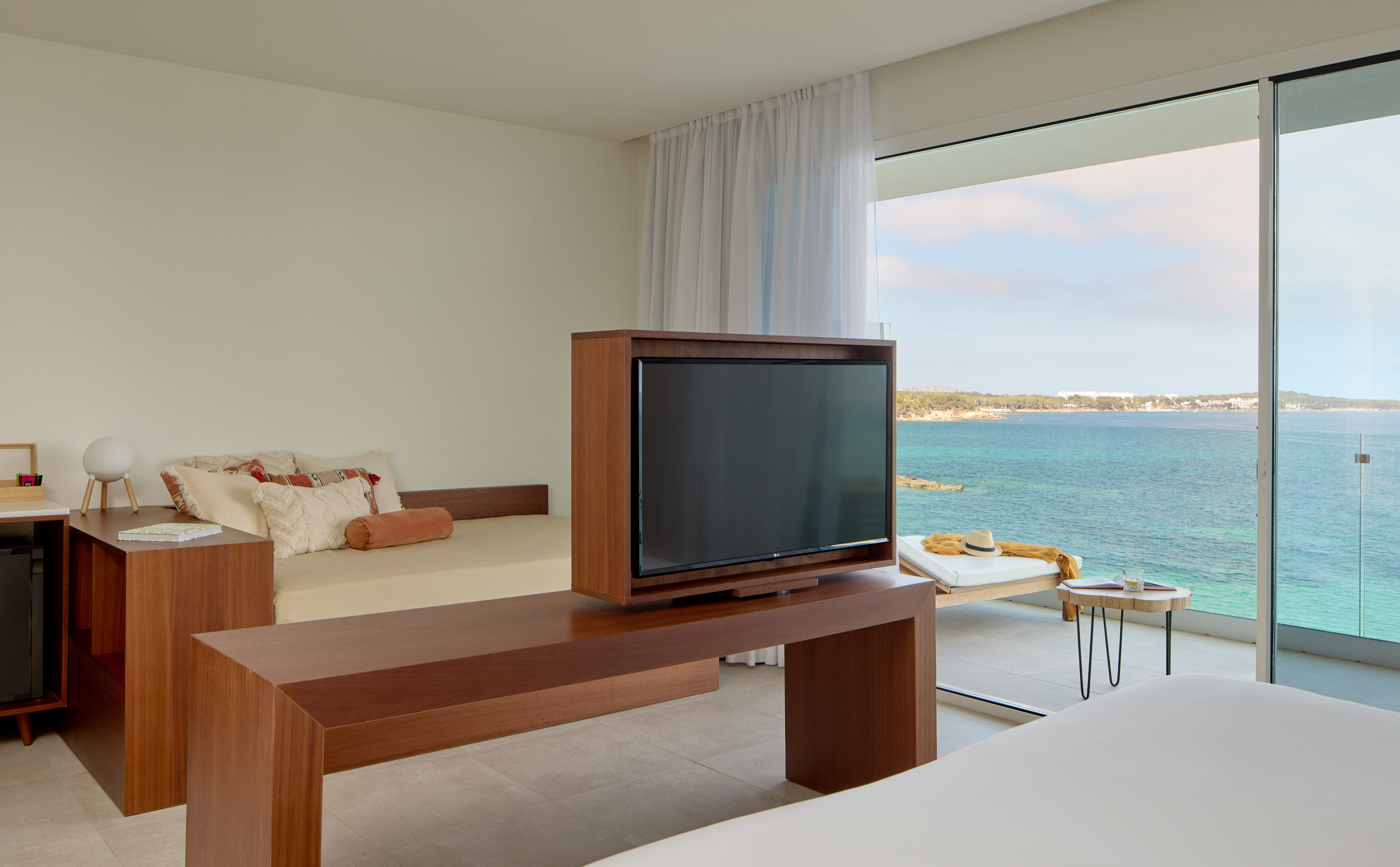 Ocean view hotel room with TV, daybed, and balcony overlooking blue sea.