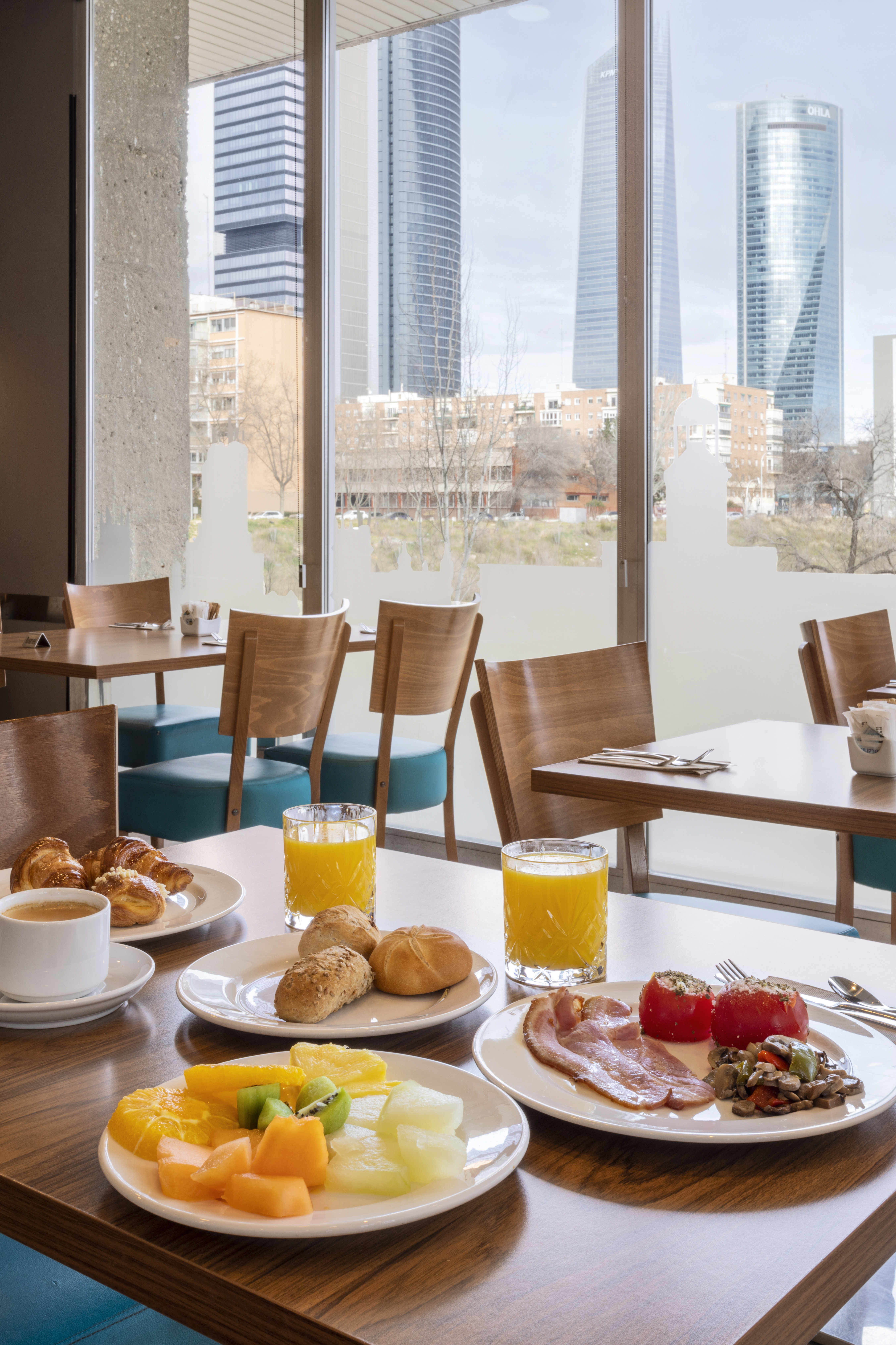 Breakfast spread with croissants, fruit, bacon, juice, and city skyline view.