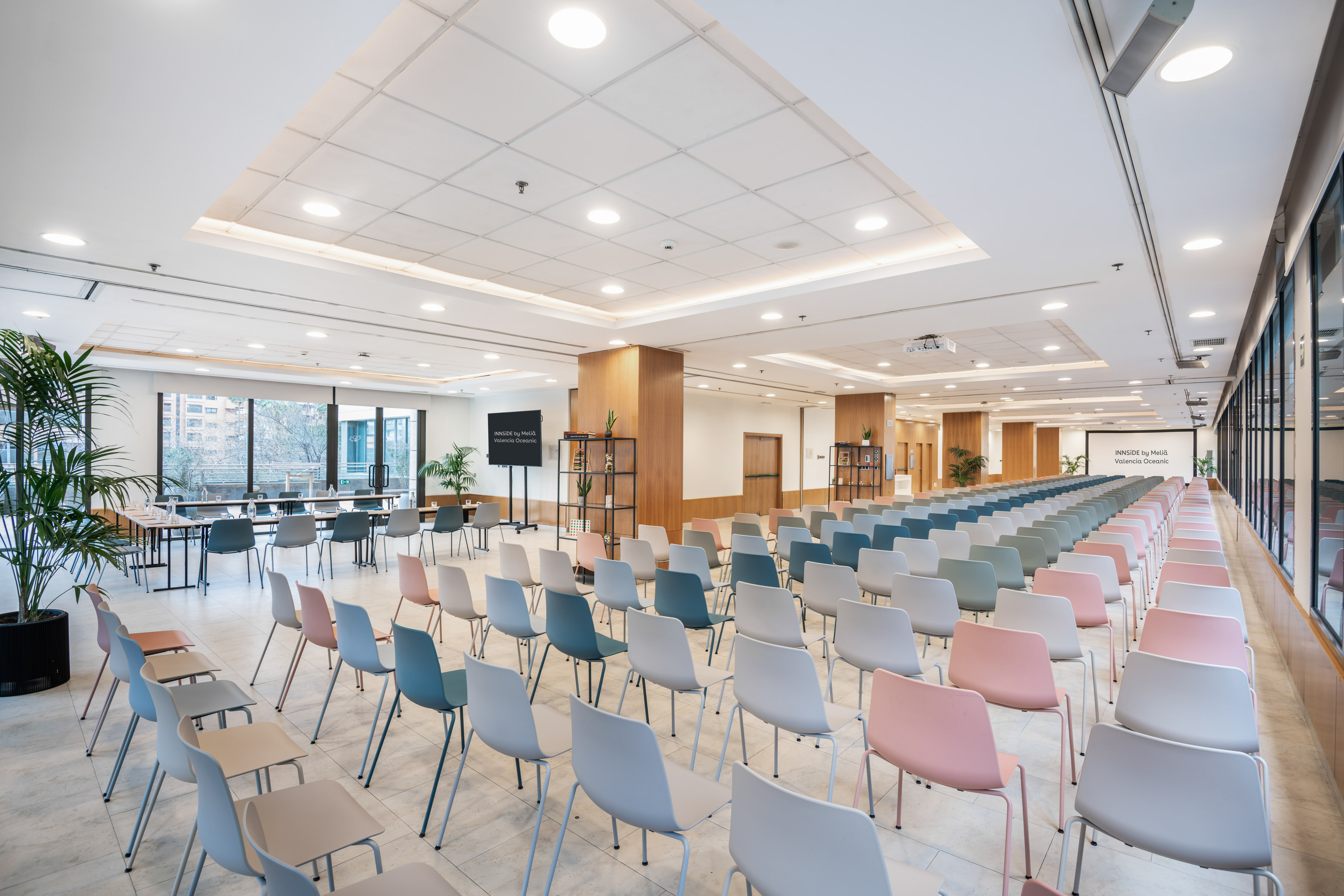 Modern hotel conference room with colorful chairs, presentation screen, and large windows.