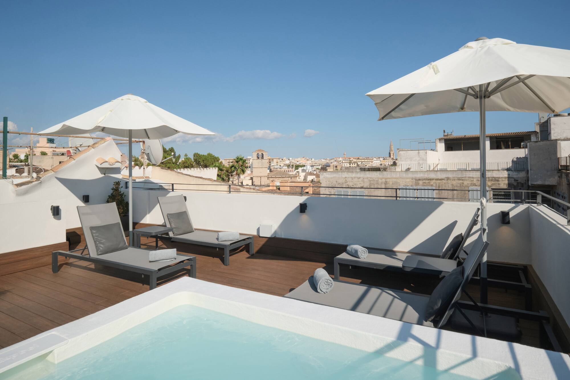 Rooftop jacuzzi terrace with sun loungers and city skyline views.