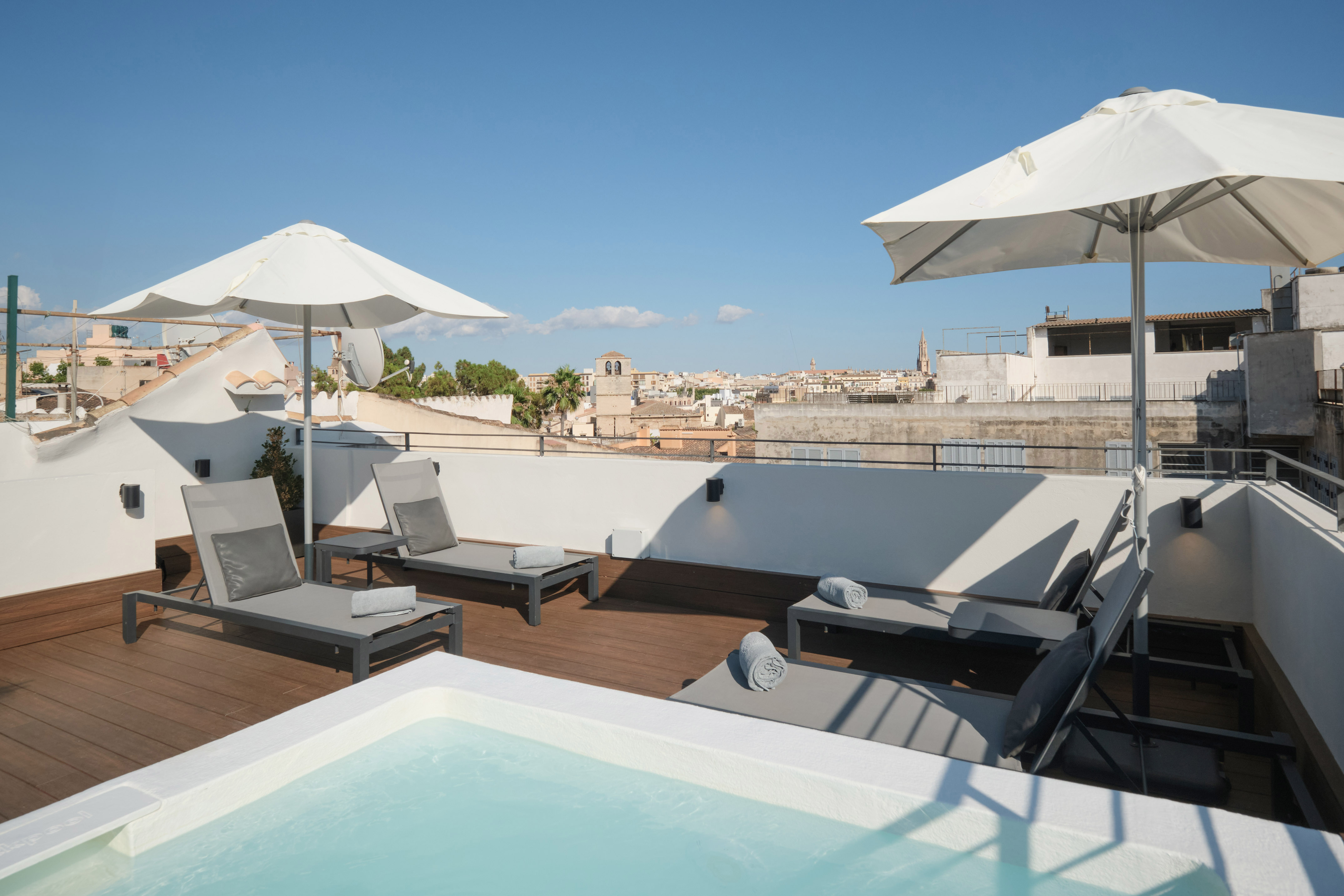 Rooftop jacuzzi terrace with sun loungers and city skyline views.