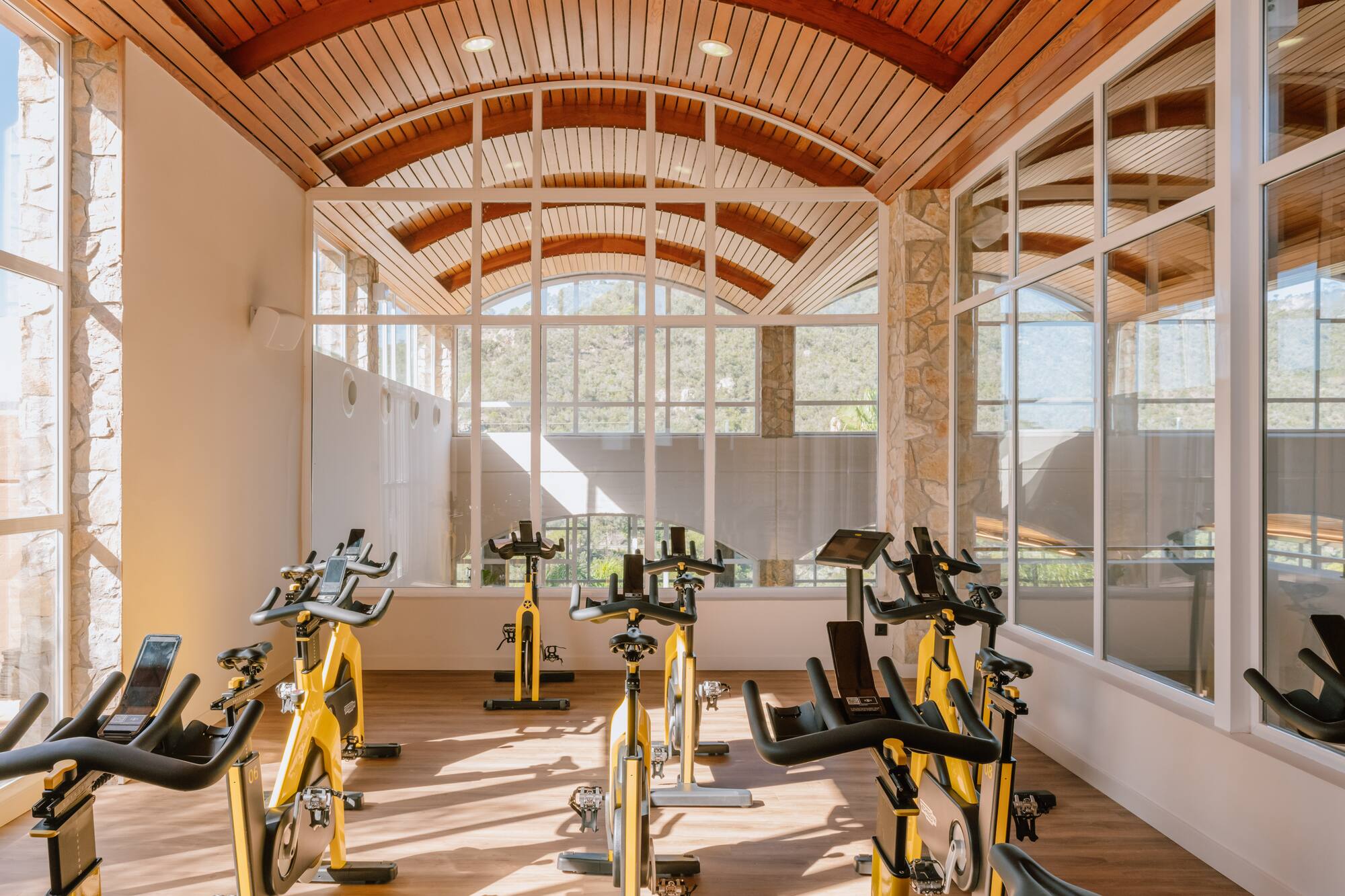 Cycling studio with yellow spin bikes, large arched windows, and a wooden ceiling.