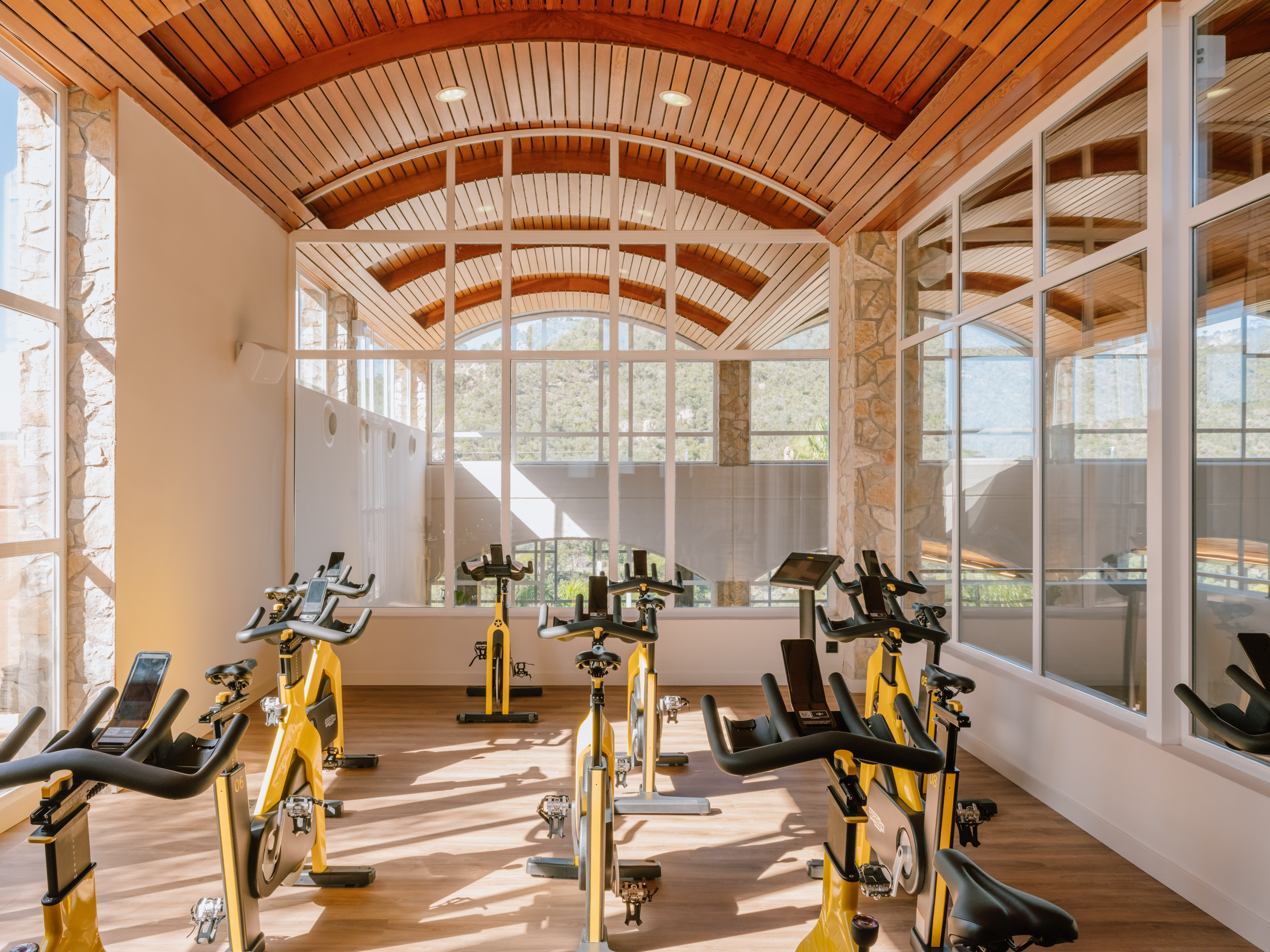 Cycling studio with yellow spin bikes, large arched windows, and a wooden ceiling.
