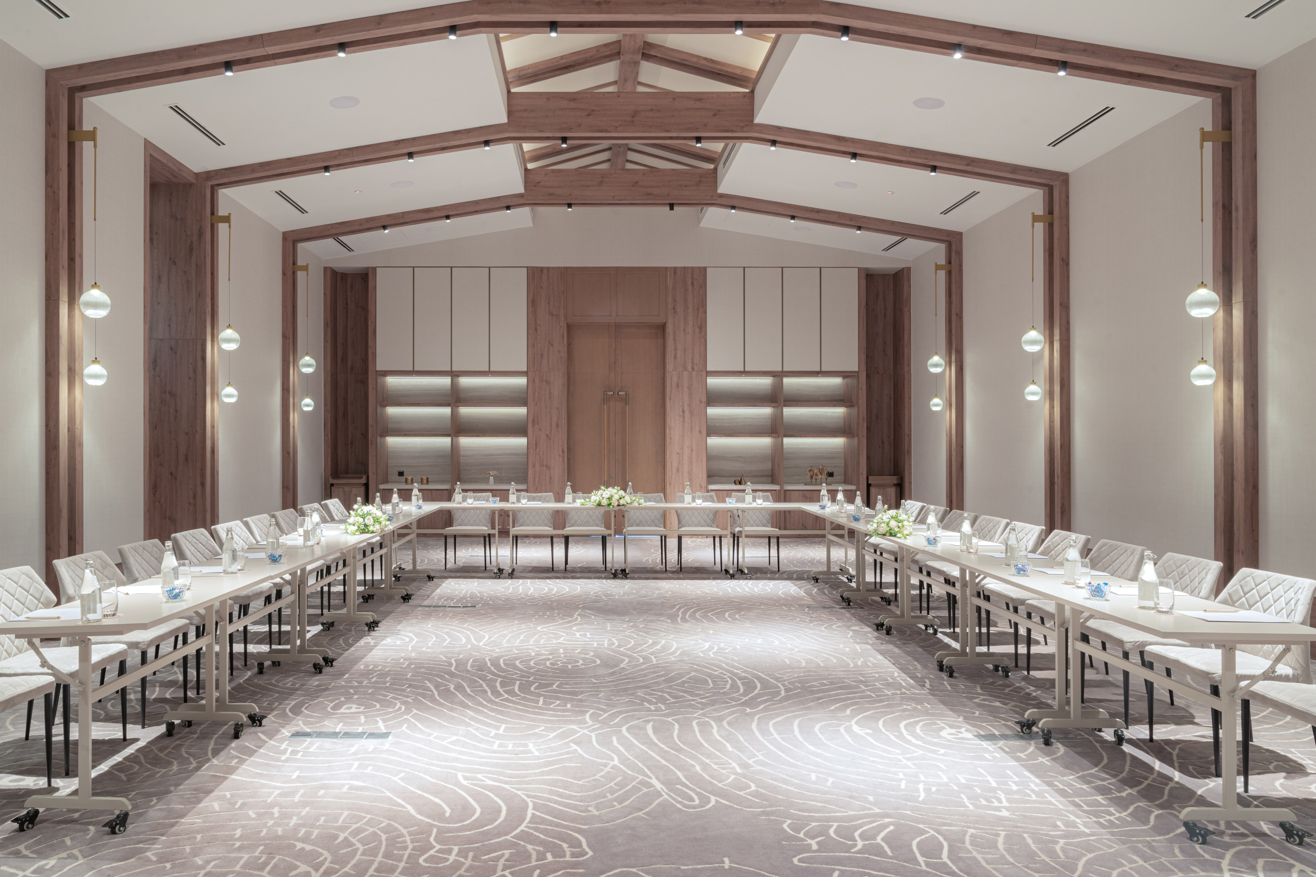 Modern conference room with U-shape tables, wooden beams, and elegant globe lighting.
