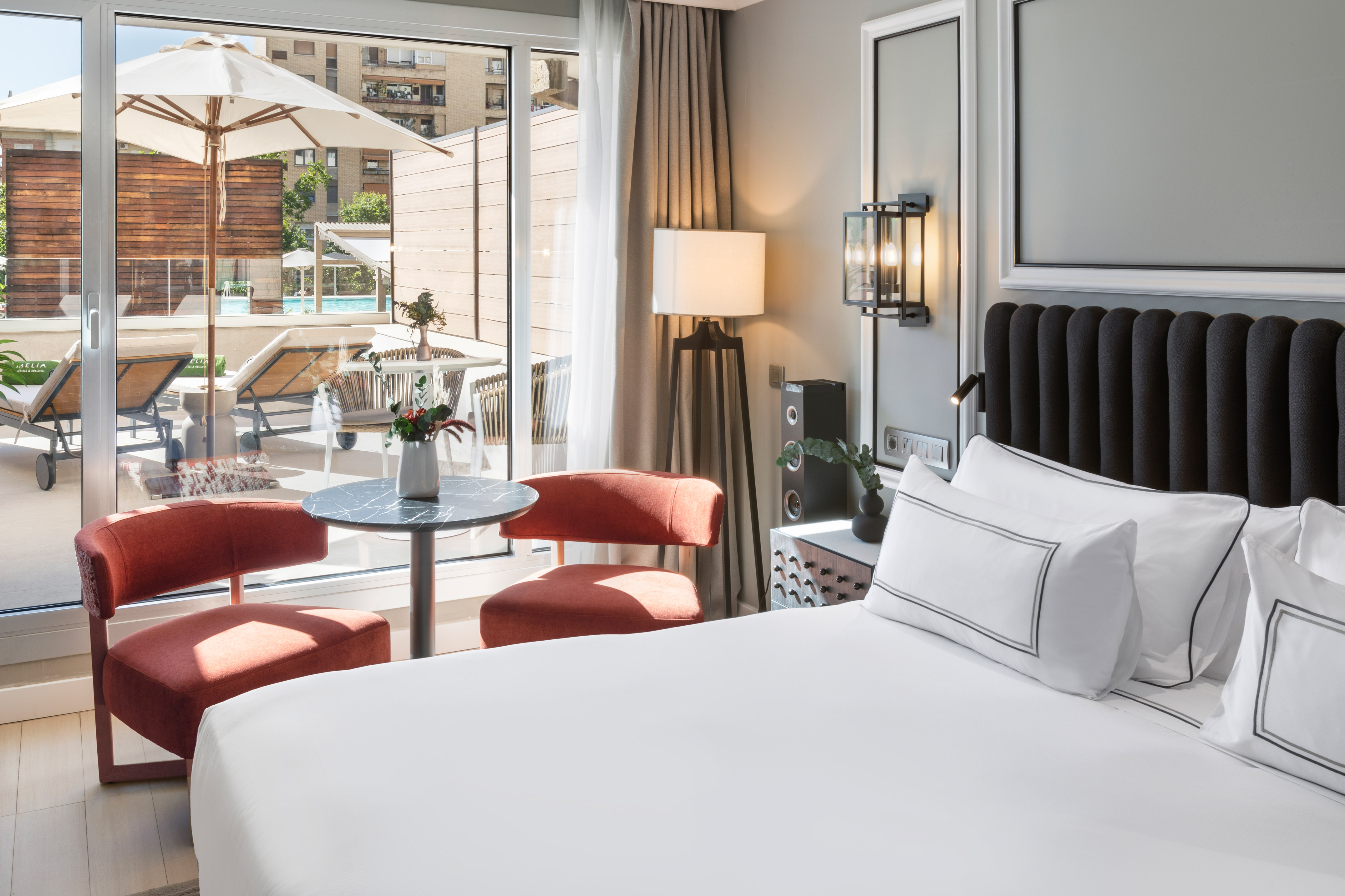 Modern hotel bedroom with bed, private terrace, pool, and stylish furnishings.