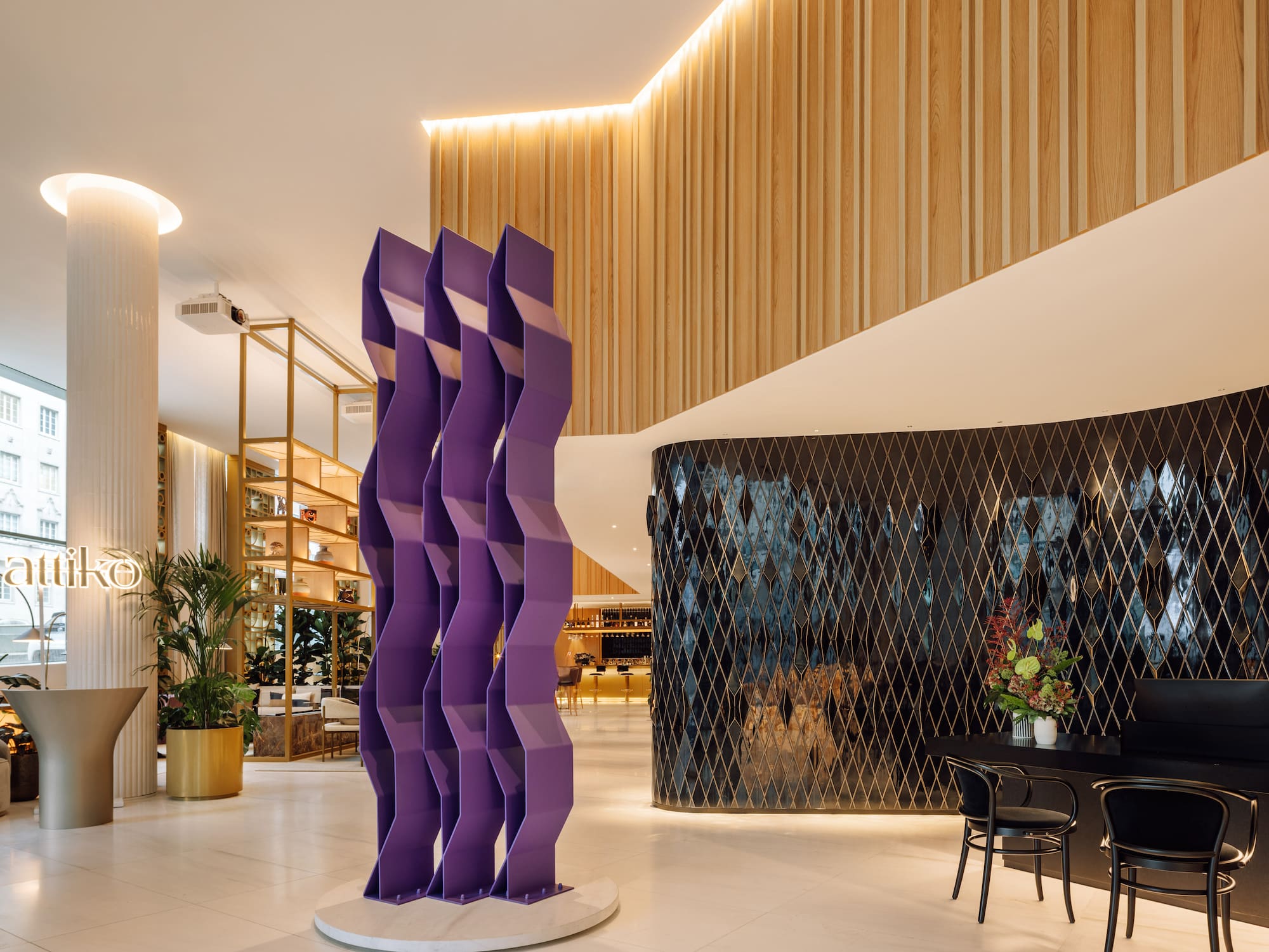 Modern hotel lobby with purple abstract sculpture, wood paneling, and black geometric wall.