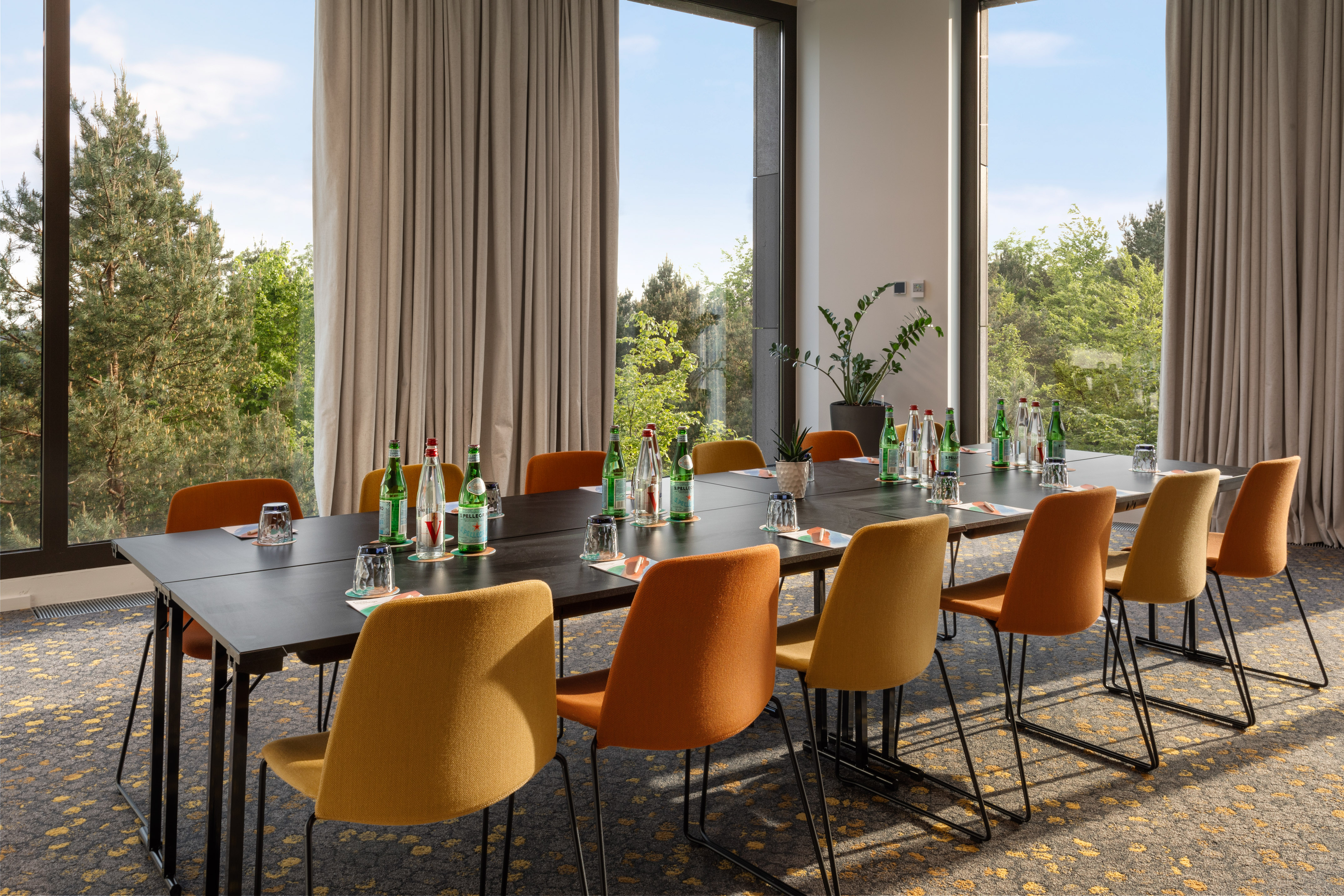 Modern meeting room with forest view, long table, and colorful chairs.