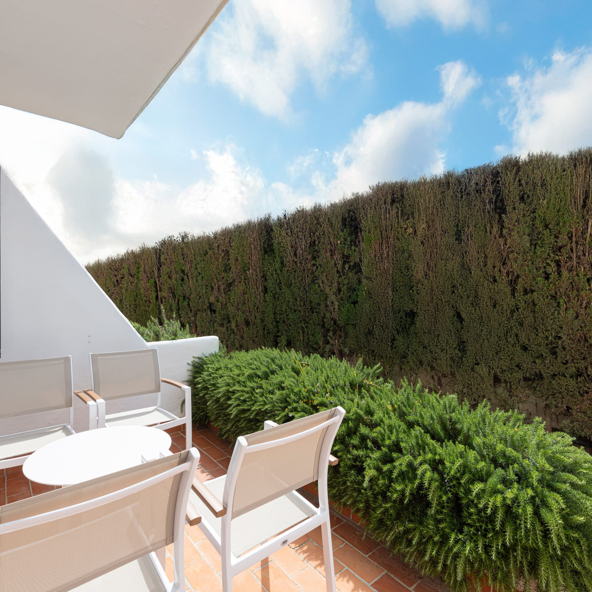 Mediterranean patio with outdoor seating, terracotta floor, and green hedge.