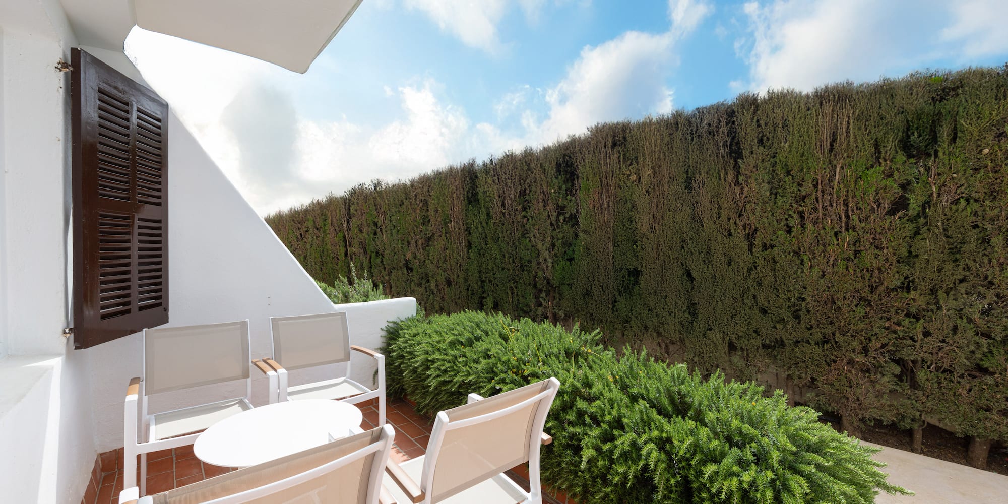 Mediterranean patio with outdoor seating, terracotta floor, and green hedge.