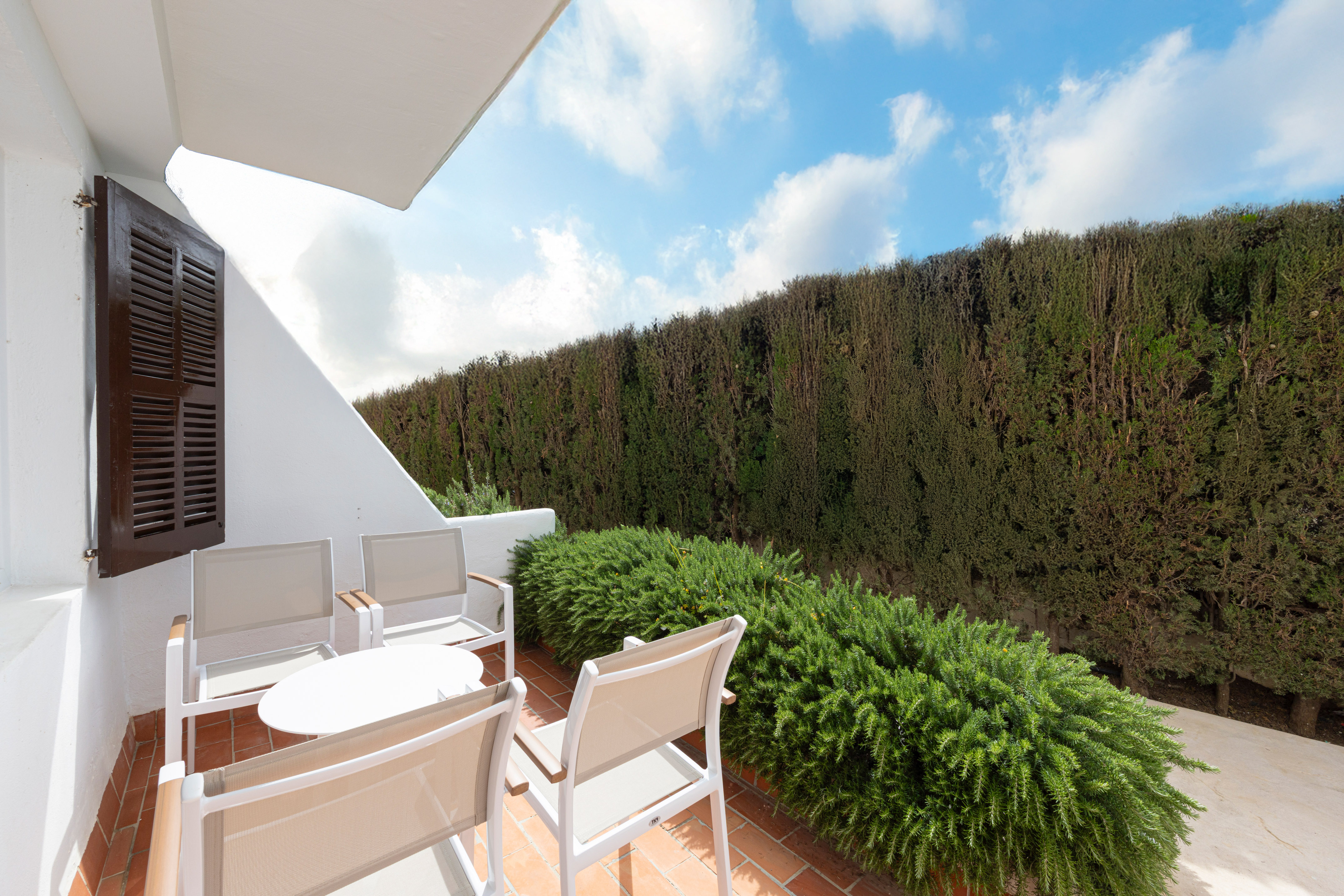 Mediterranean patio with outdoor seating, terracotta floor, and green hedge.