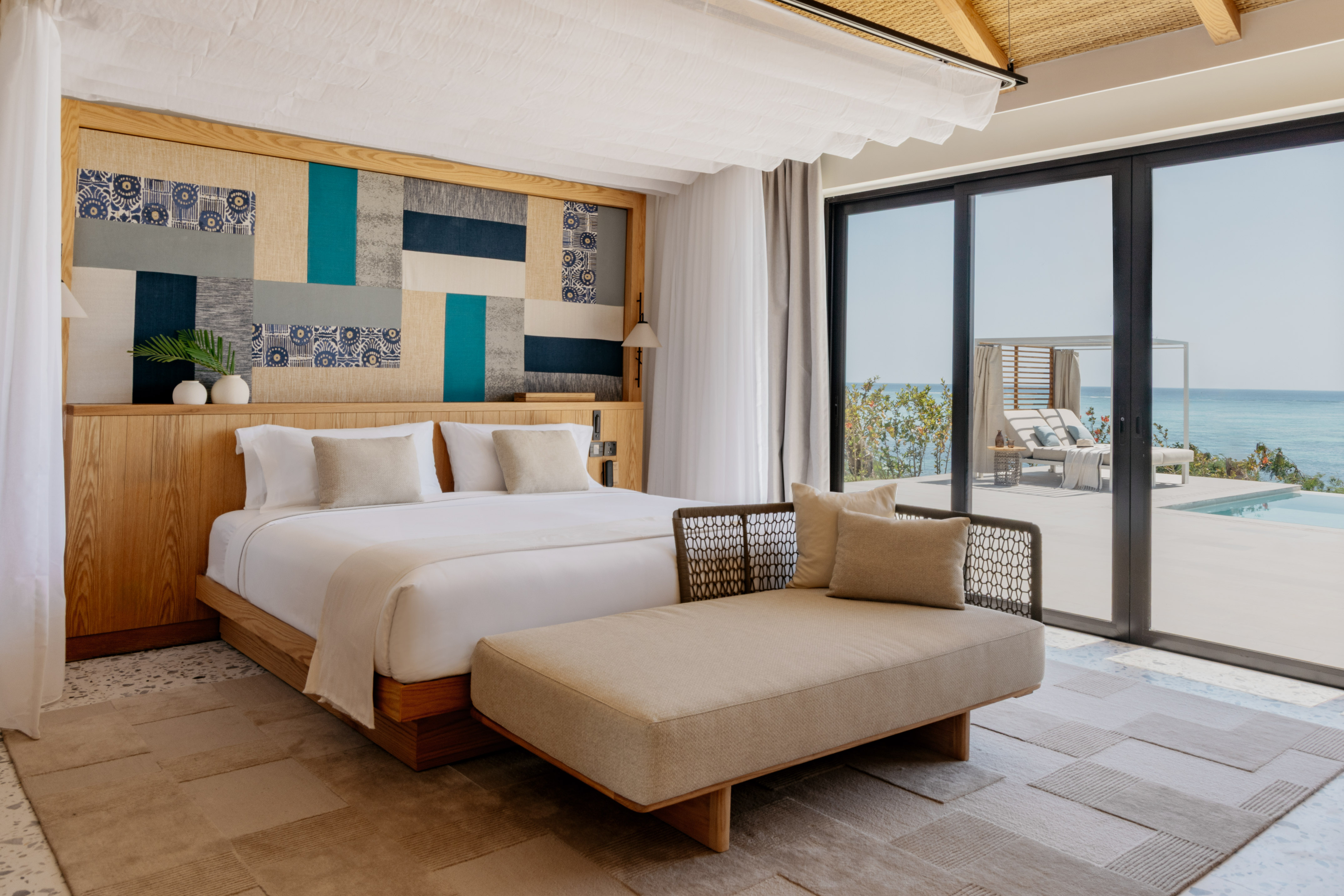 Luxury hotel bedroom with patterned headboard, ocean view, and private pool.