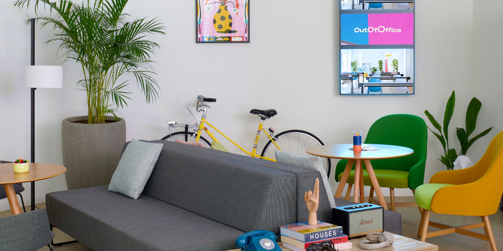 Lounge de oficina moderno con sofá, sillas coloridas, plantas y bicicleta.