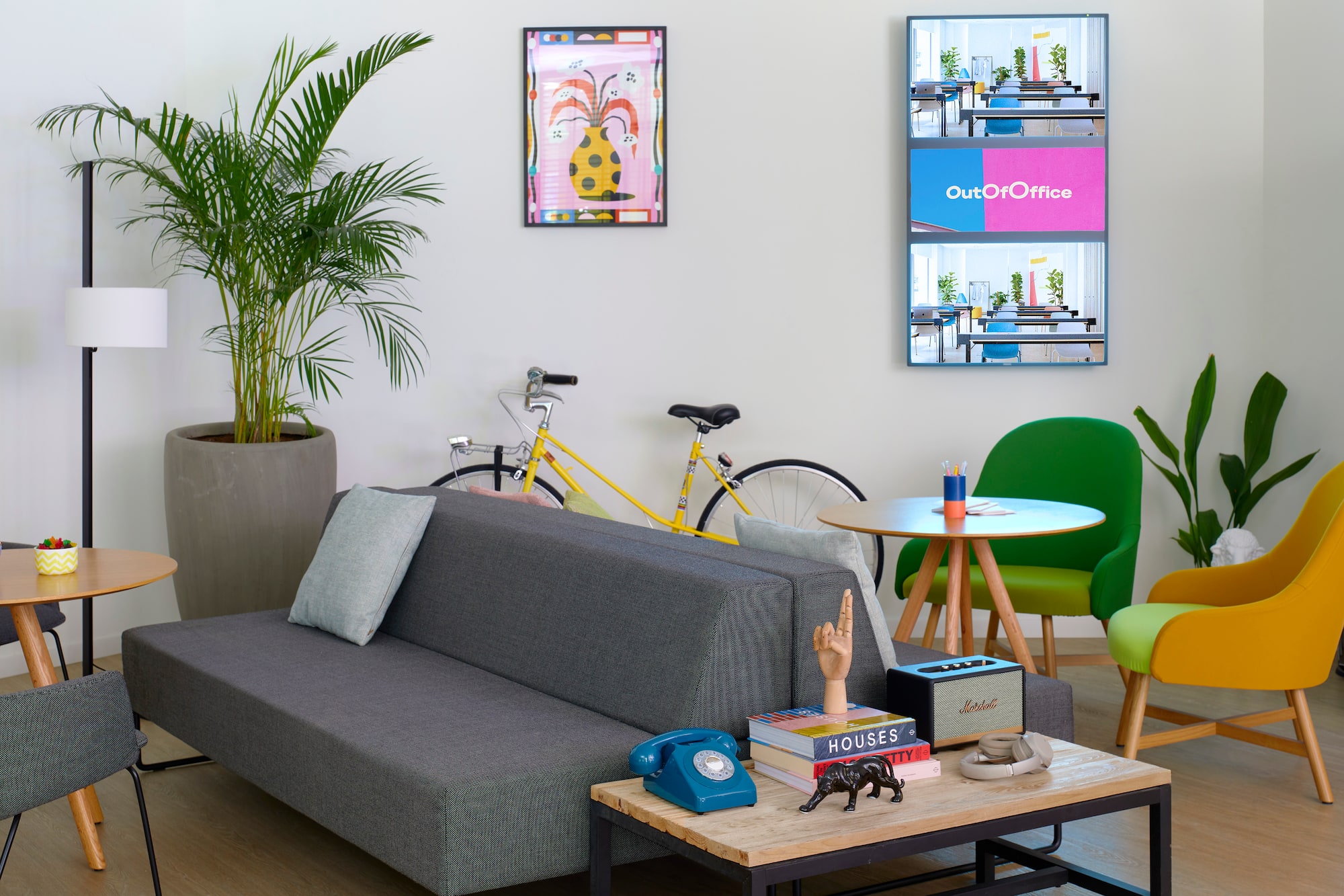 Lounge de oficina moderno con sofá, sillas coloridas, plantas y bicicleta.