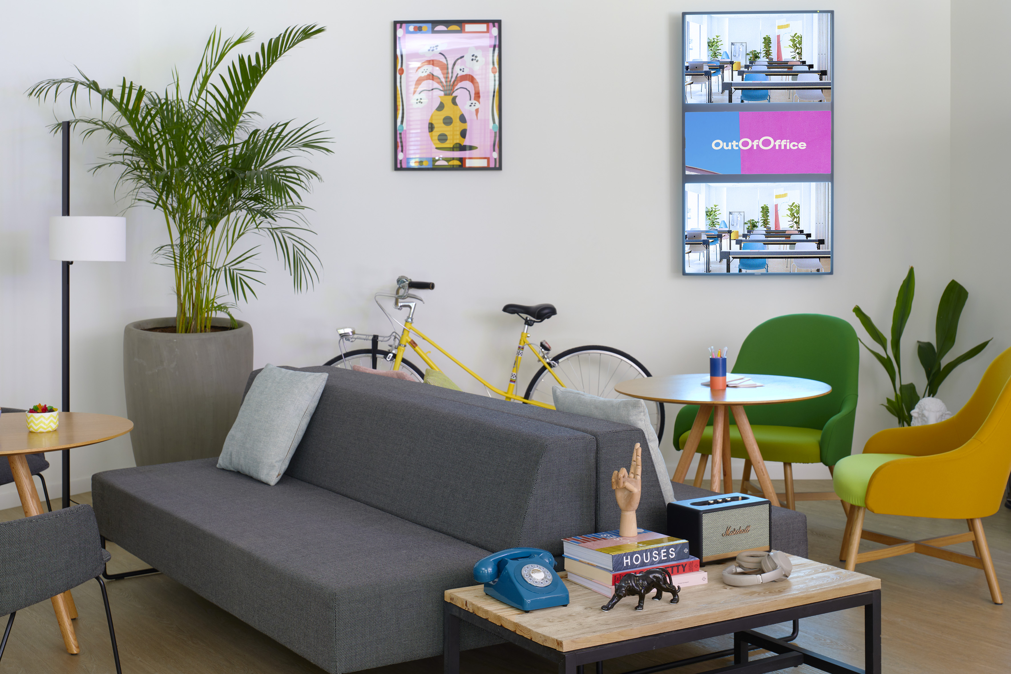 Lounge de oficina moderno con sofá, sillas coloridas, plantas y bicicleta.