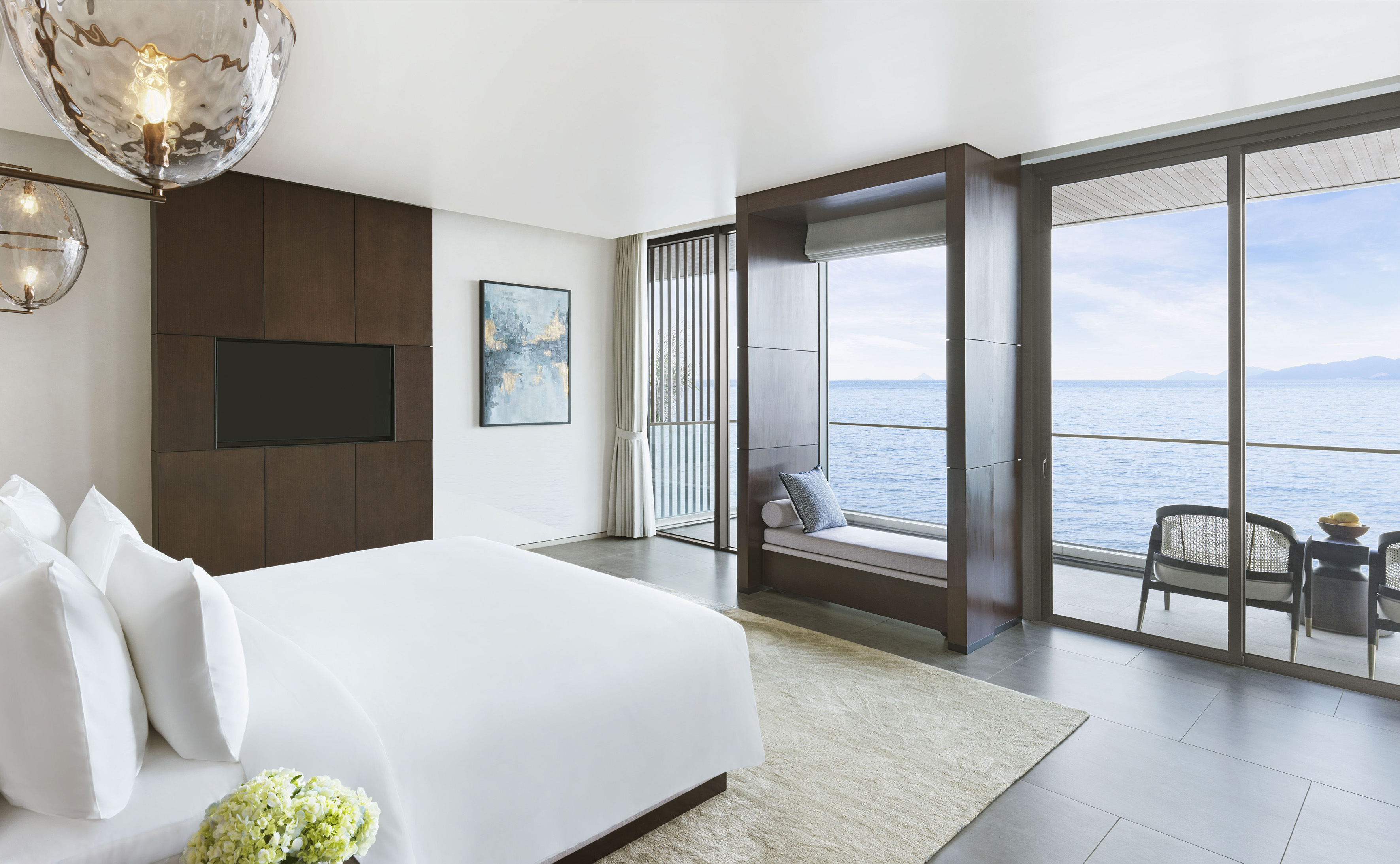 Modern hotel bedroom with ocean view, white bed, and window seat.