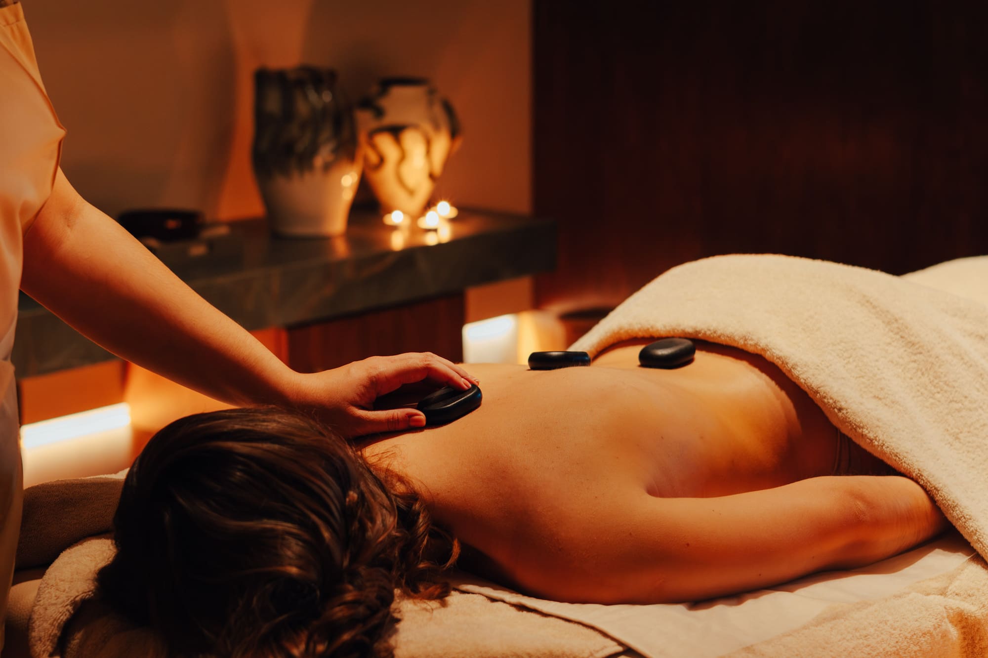 Woman receiving hot stone back massage in a dimly lit spa.