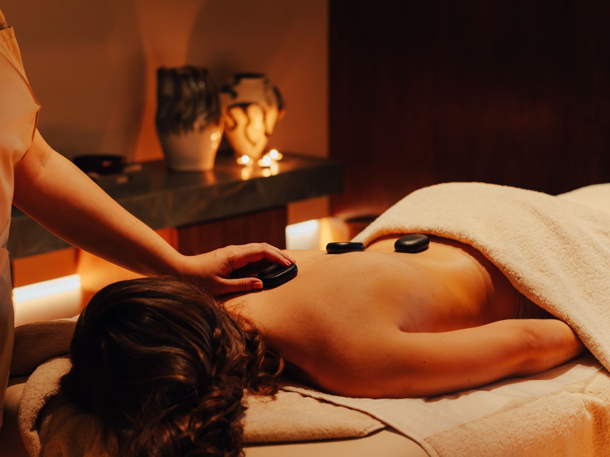 Masseuse applying hot stone massage to woman's back in a tranquil spa.