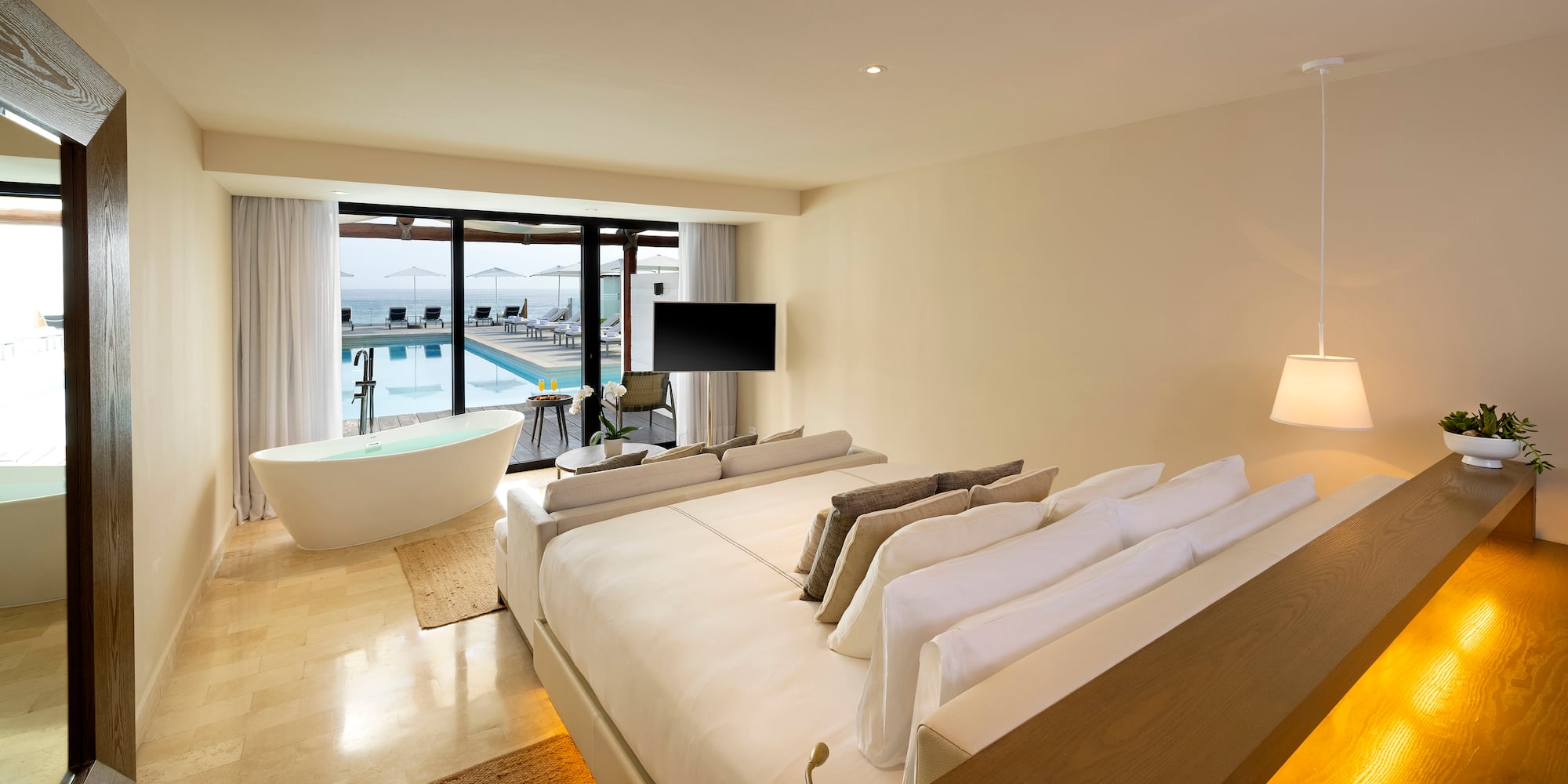 a room with a large bed and a tub with a pool in the background