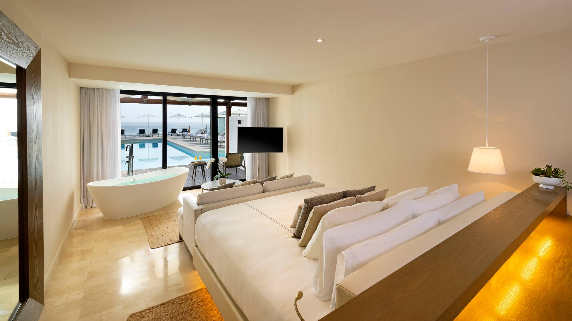 a room with a large bed and a tub with a pool in the background