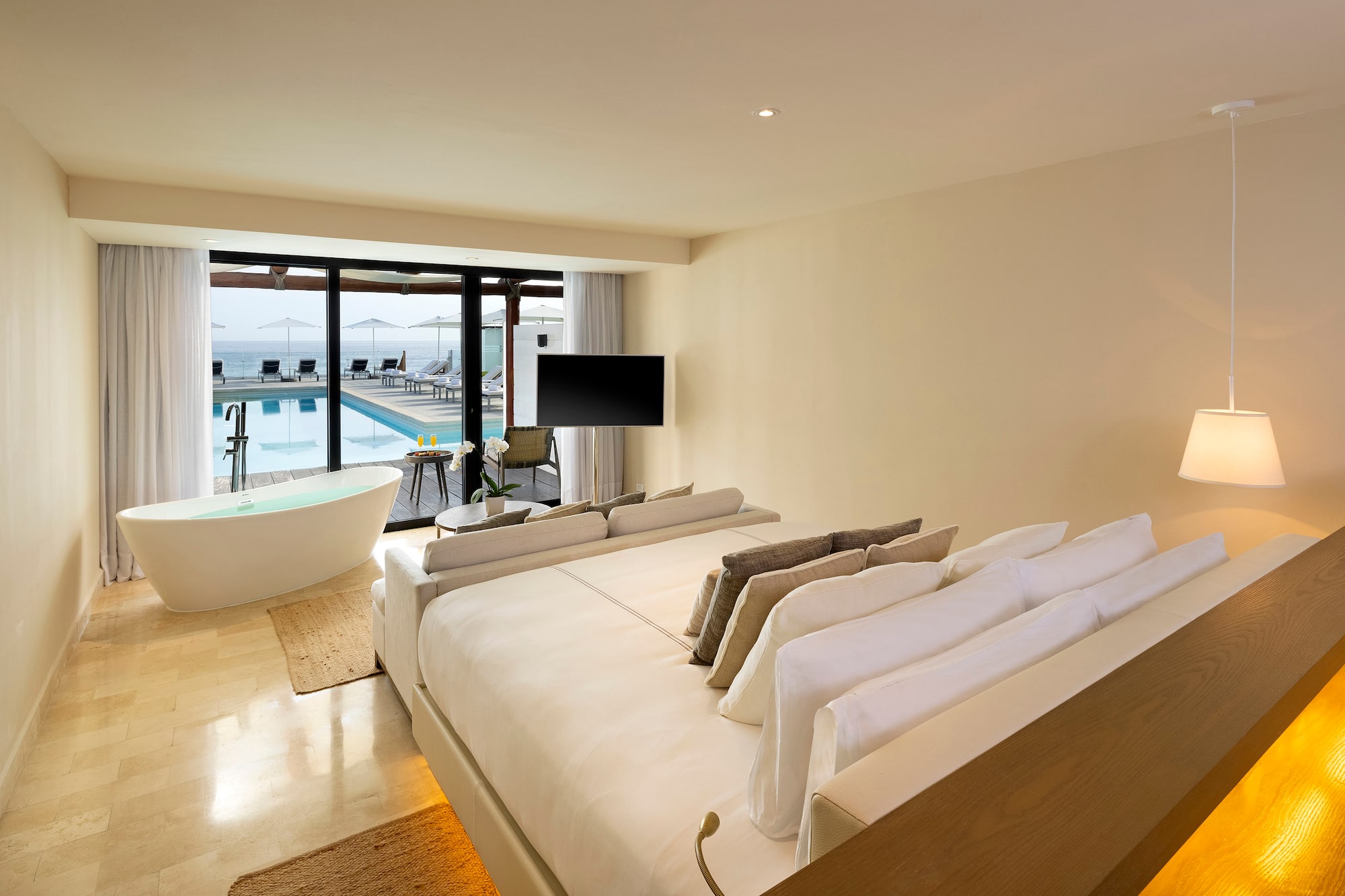 a room with a large bed and a tub with a pool in the background