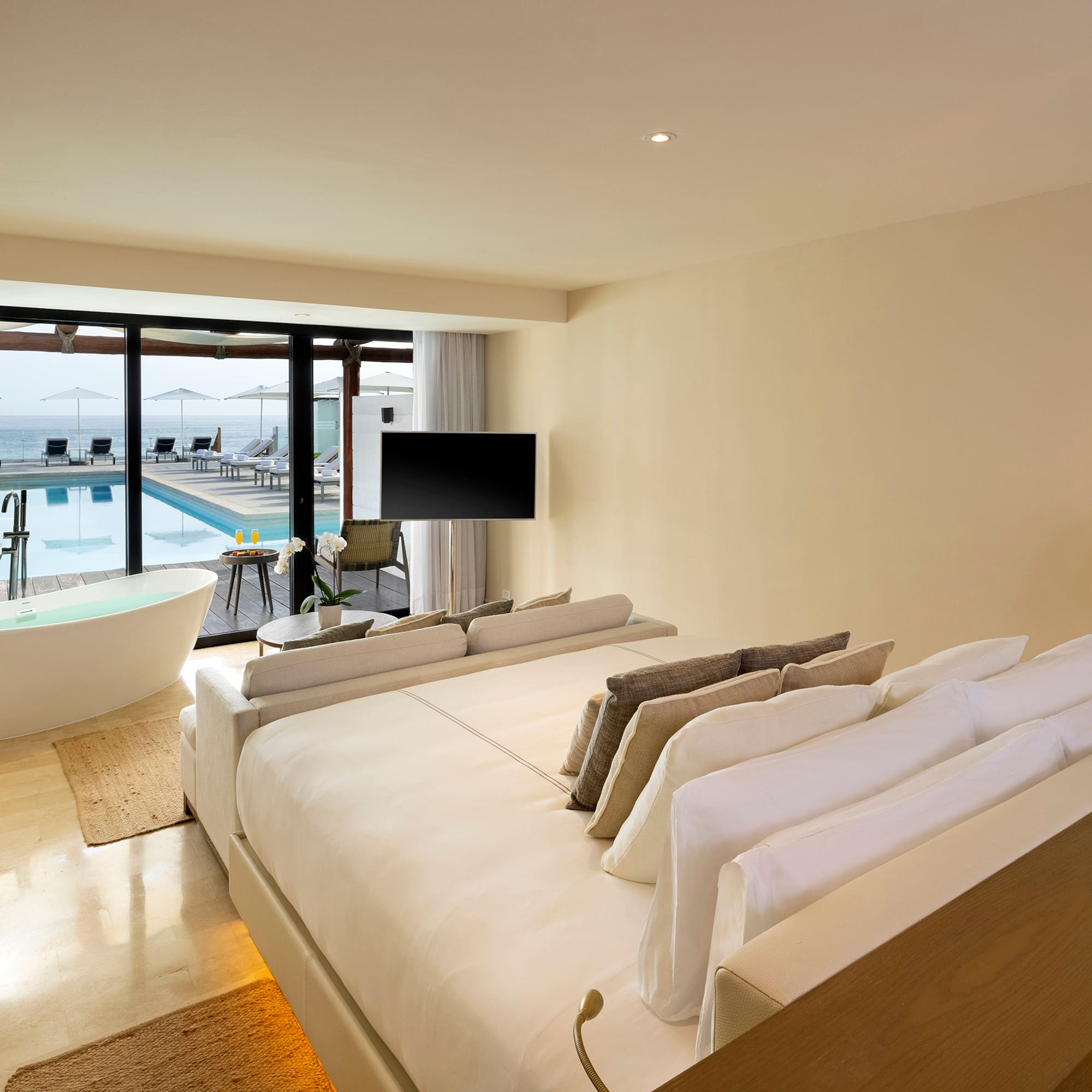 a room with a large bed and a tub with a pool in the background