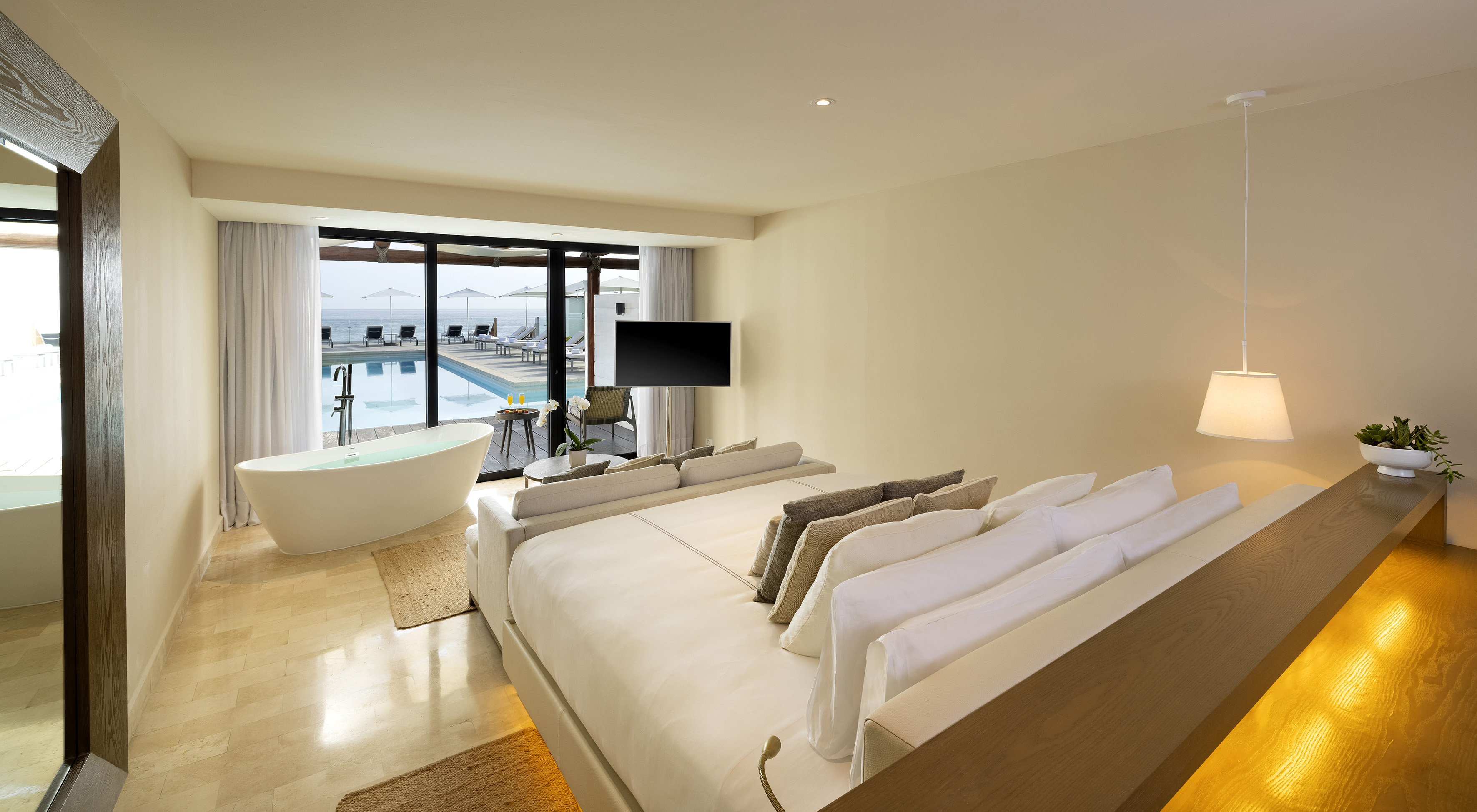Luxury hotel suite with poolside ocean view, large bed, and freestanding bathtub.