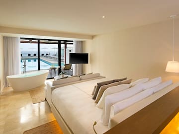 a room with a large bed and a tub with a pool in the background