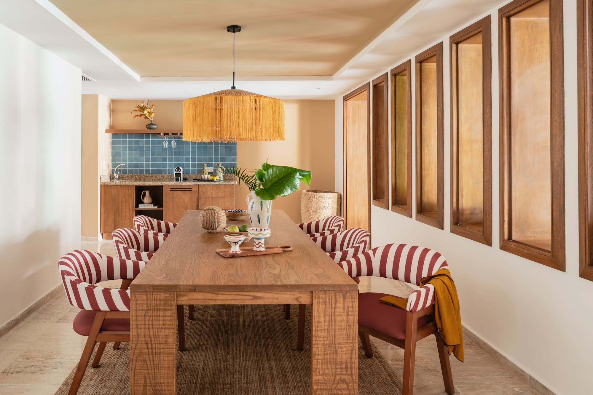 Modern dining room with wood table, red striped chairs, rattan light, kitchenette.