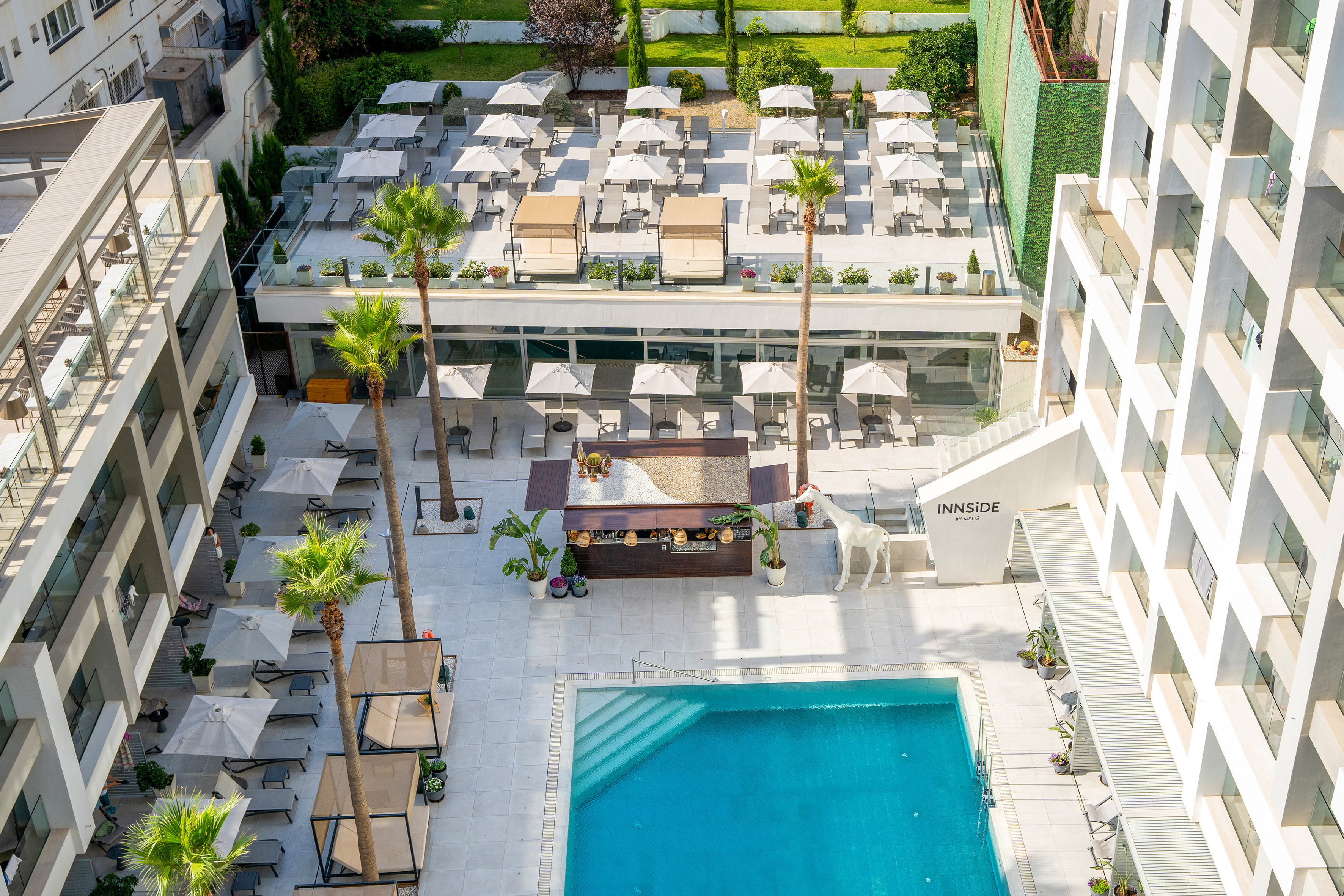INNSiDE hotel pool area with lounge chairs, outdoor restaurant, and palm trees.