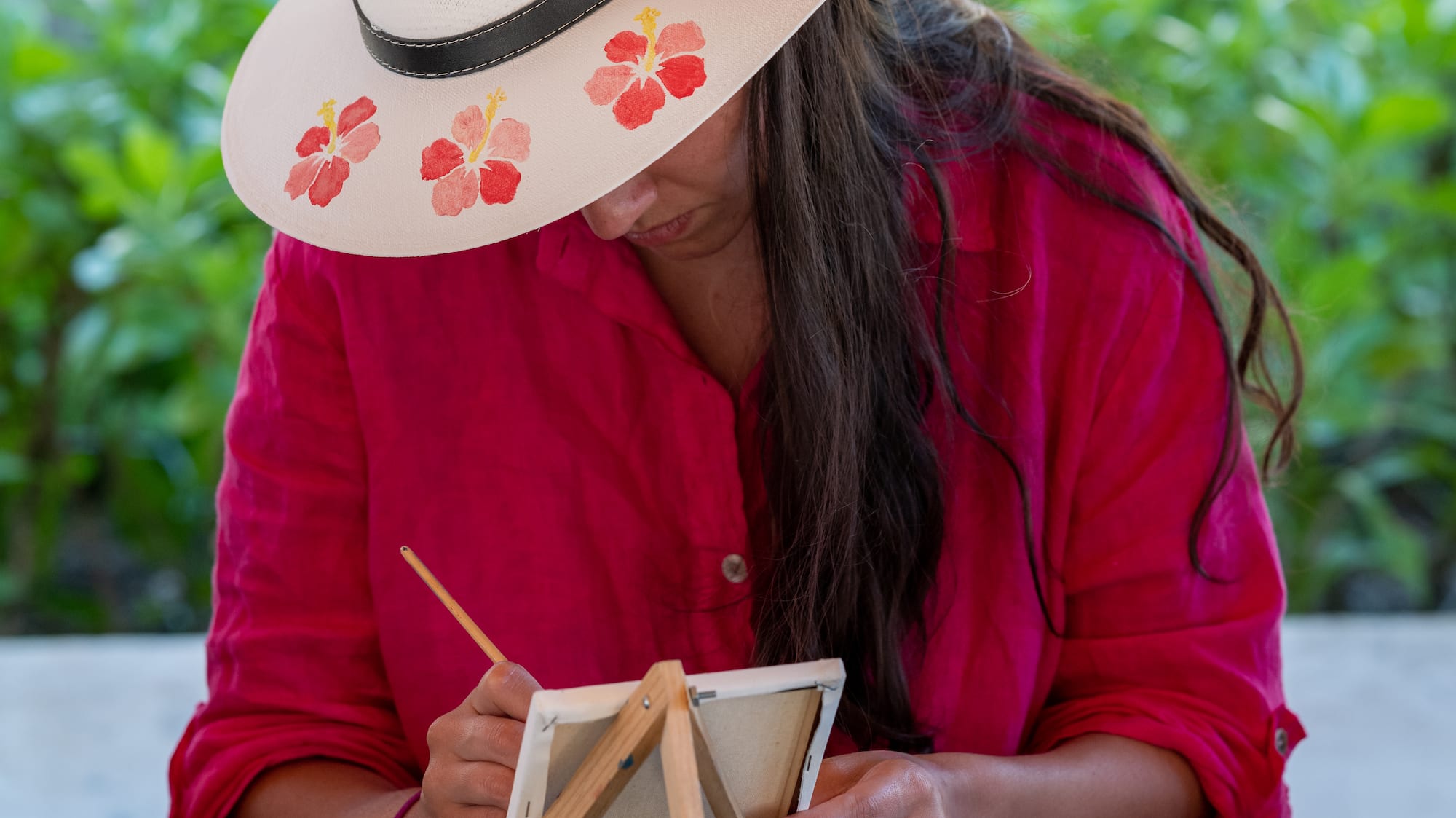 a woman wearing a hat and painting on a small easel