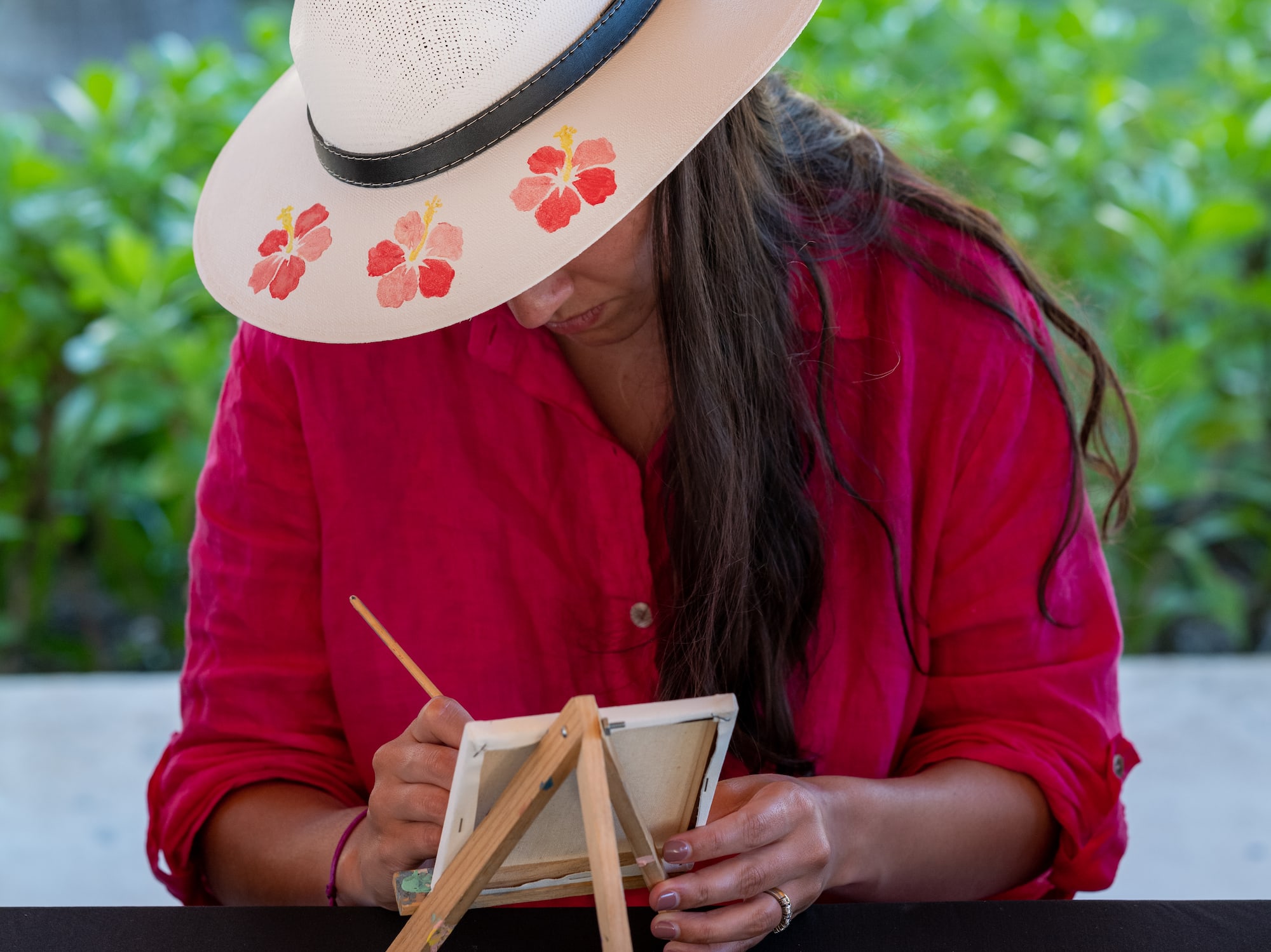 a woman wearing a hat and painting on a small easel