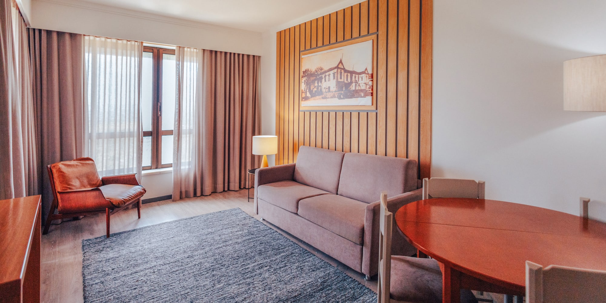 Hotel suite living room with sofa, armchair, dining area, wood accent wall.