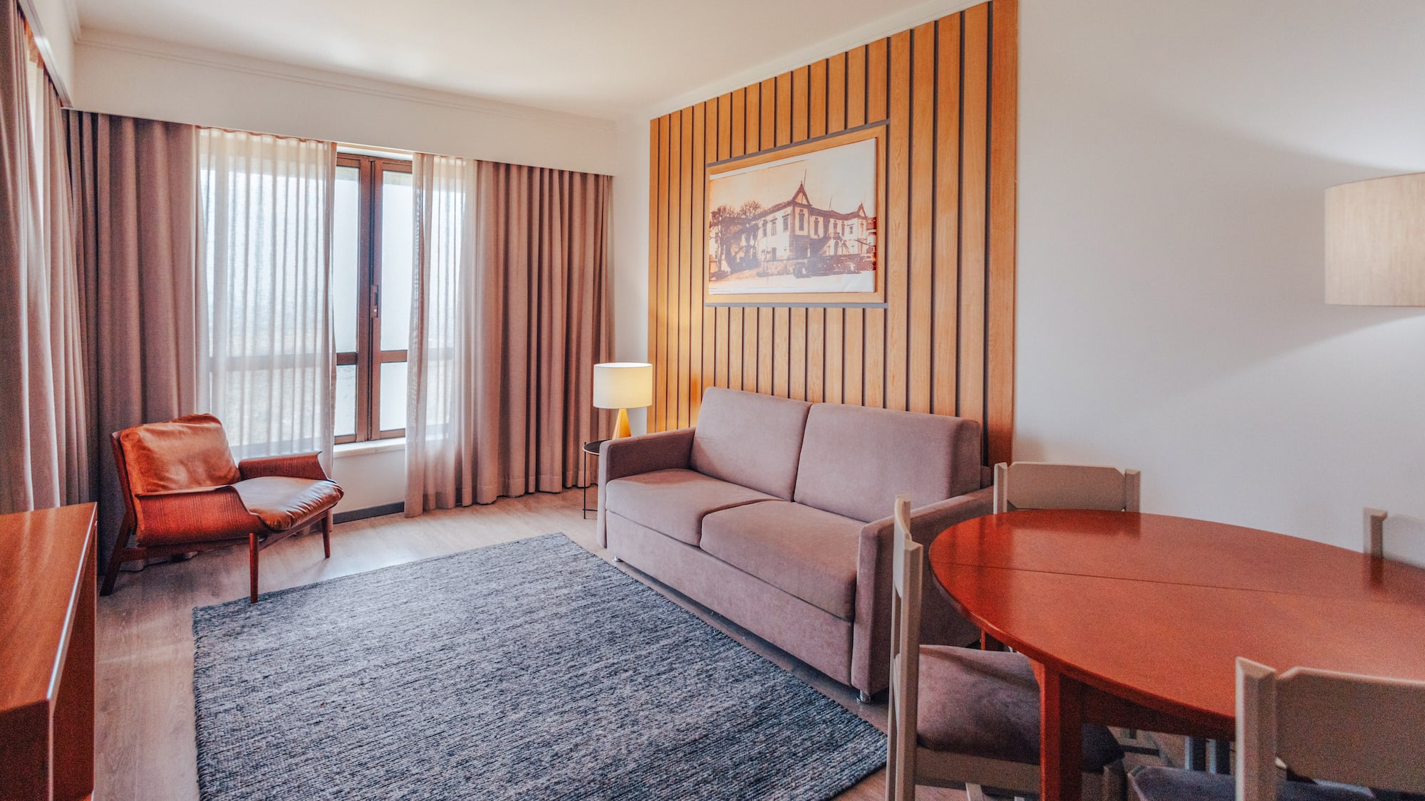 Hotel suite living room with sofa, armchair, dining area, wood accent wall.