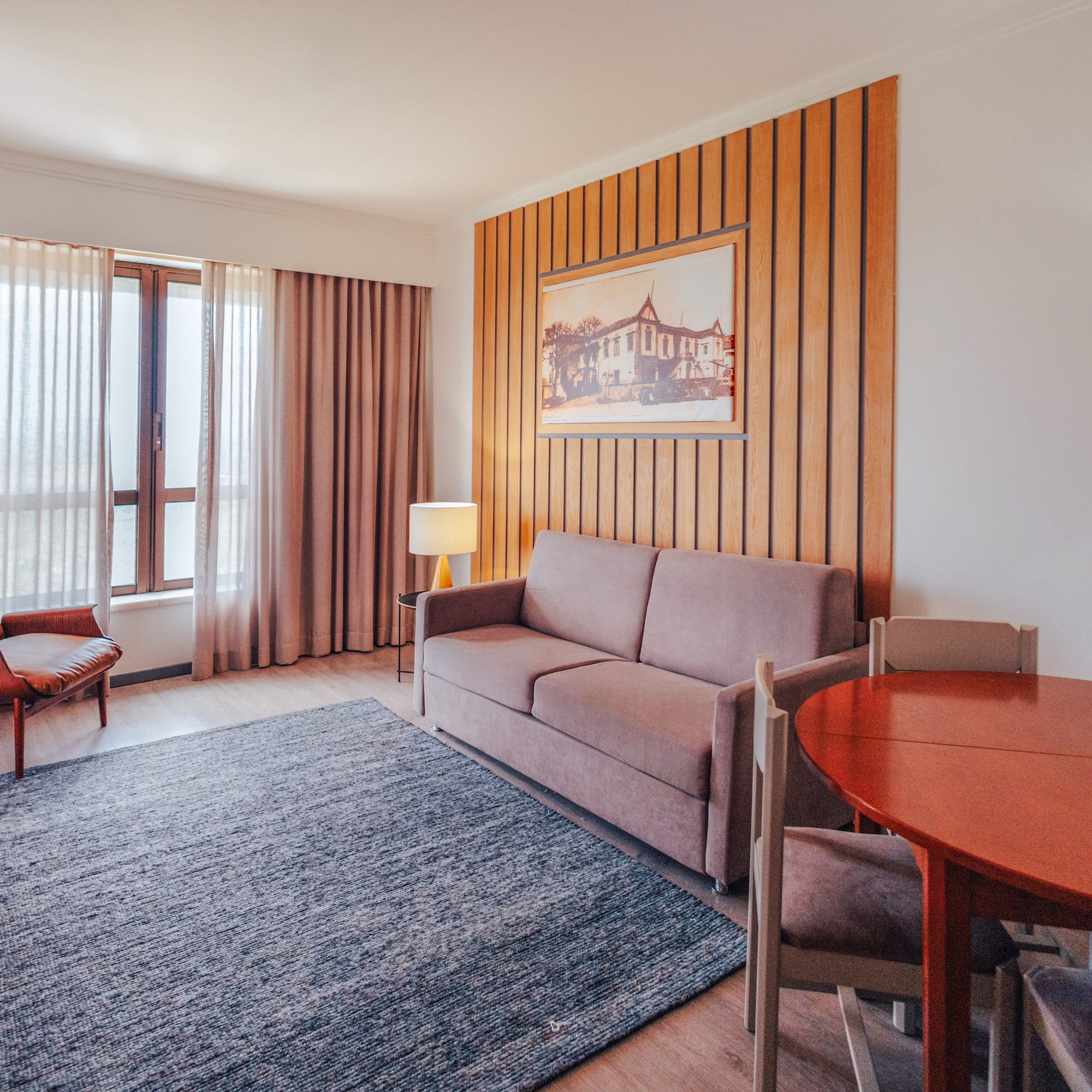 Hotel suite living room with sofa, armchair, dining area, wood accent wall.