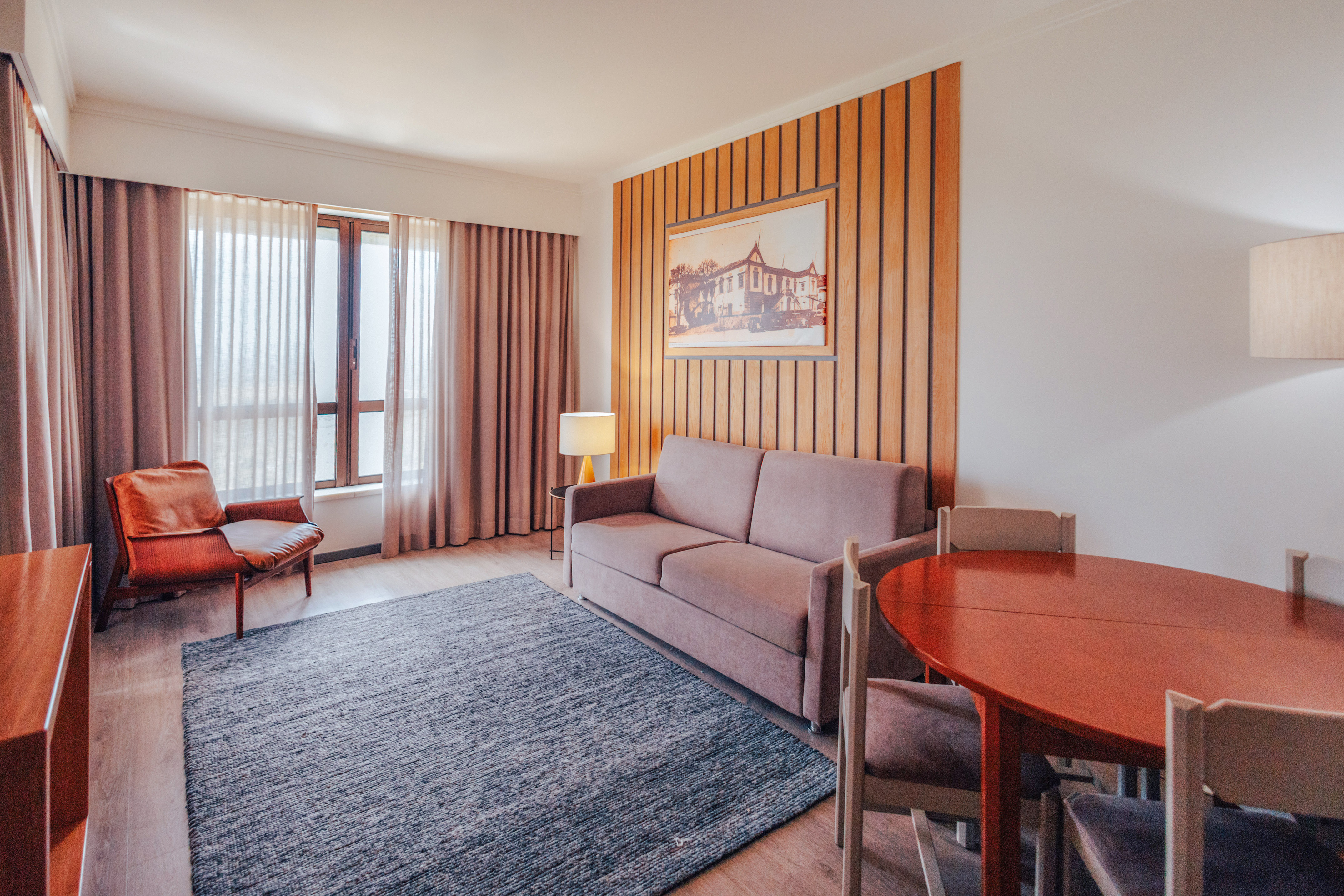 Hotel suite living room with sofa, armchair, dining area, wood accent wall.