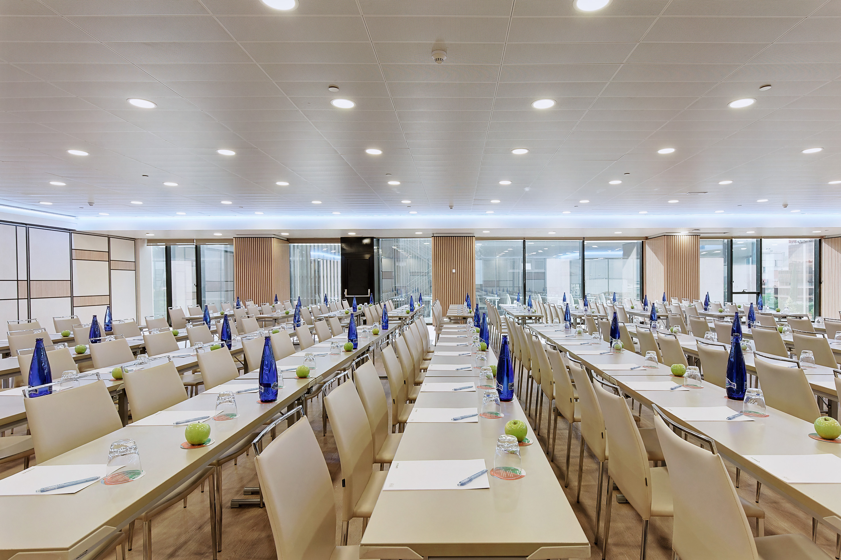 Bright, modern conference room for events, with tables, chairs, water, apples.