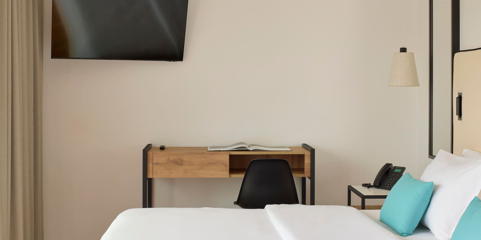 a bed with a blue pillow and a desk and a television on the wall
