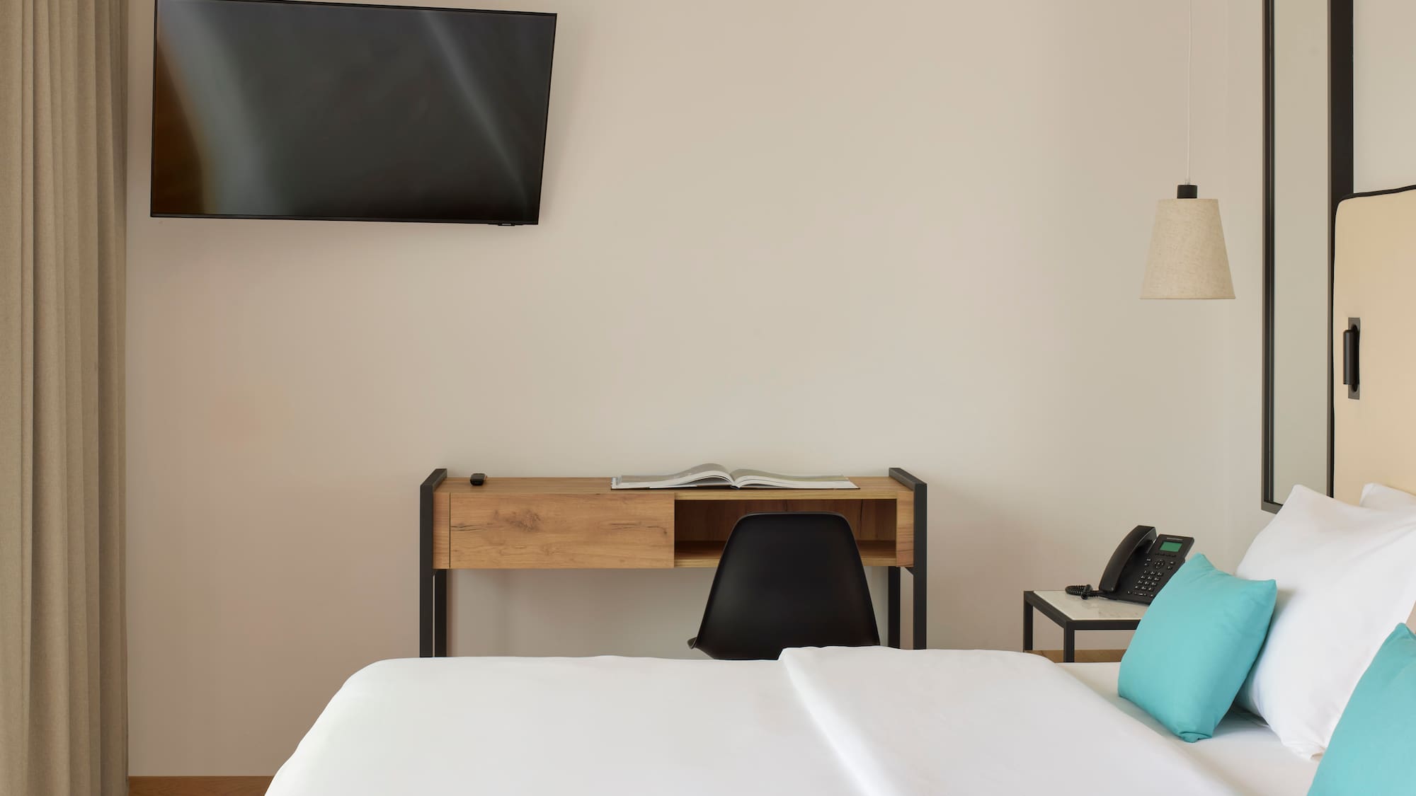 a bed with a blue pillow and a desk and a television on the wall