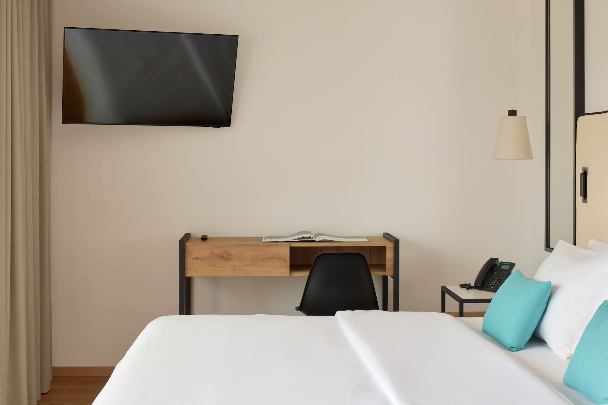 a bed with a blue pillow and a desk and a television on the wall