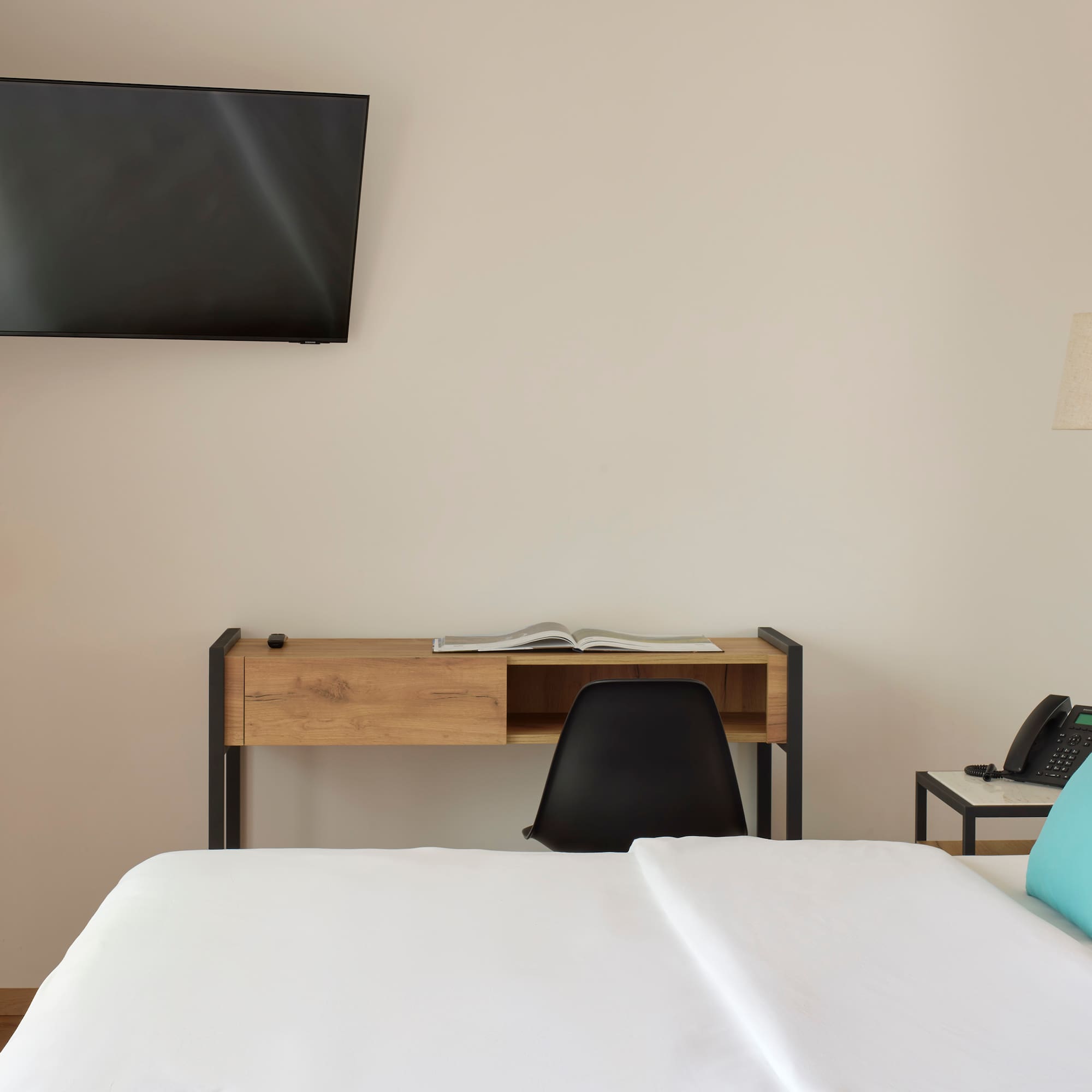 a bed with a blue pillow and a desk and a television on the wall