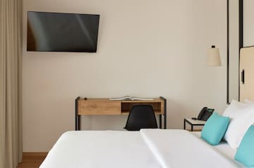 a bed with a blue pillow and a desk and a television on the wall