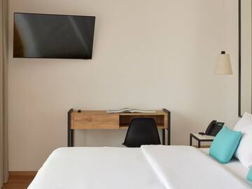 a bed with a blue pillow and a desk and a television on the wall