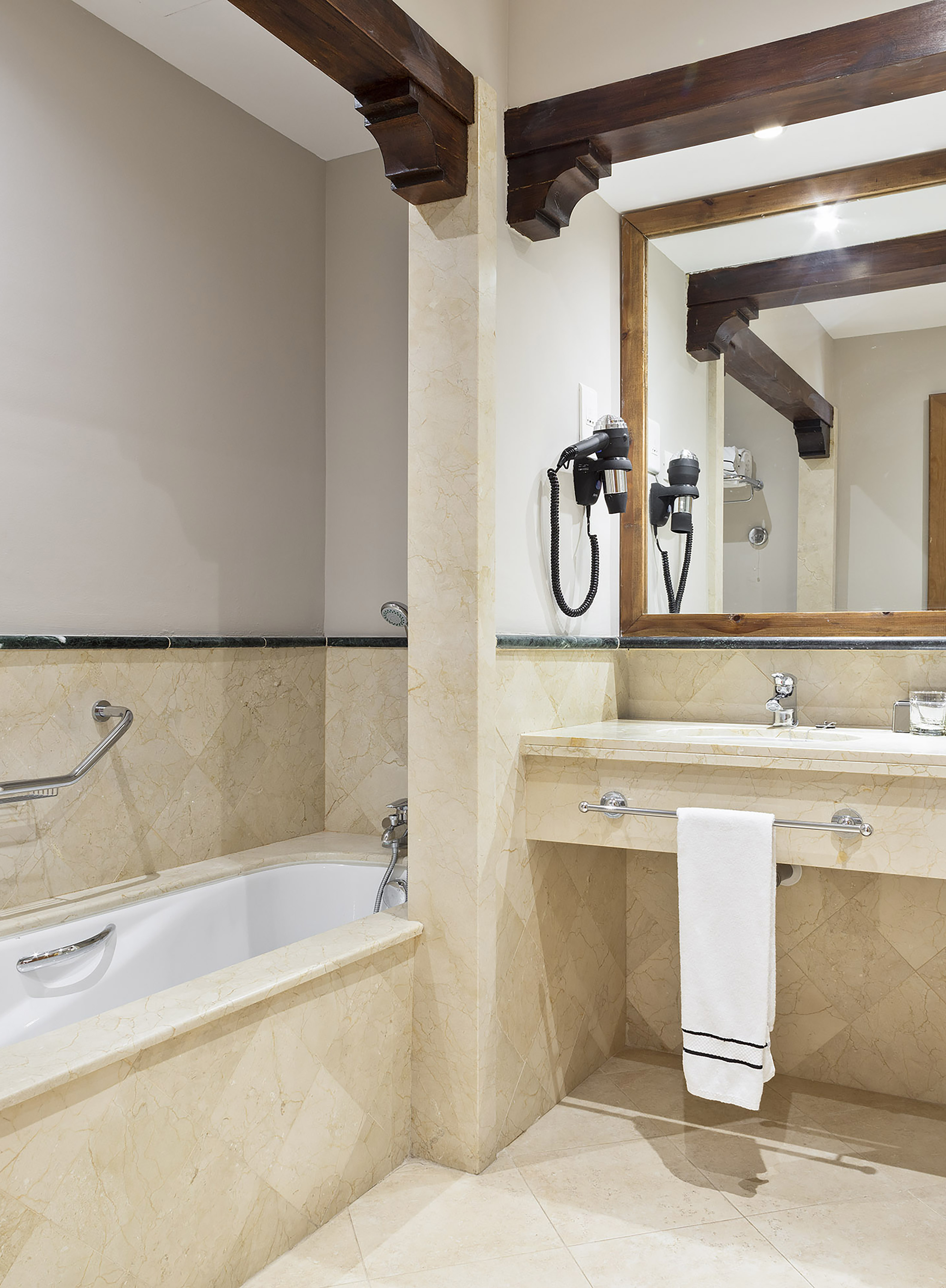Elegant marble bathroom with rustic wooden beams, bathtub, and vanity.