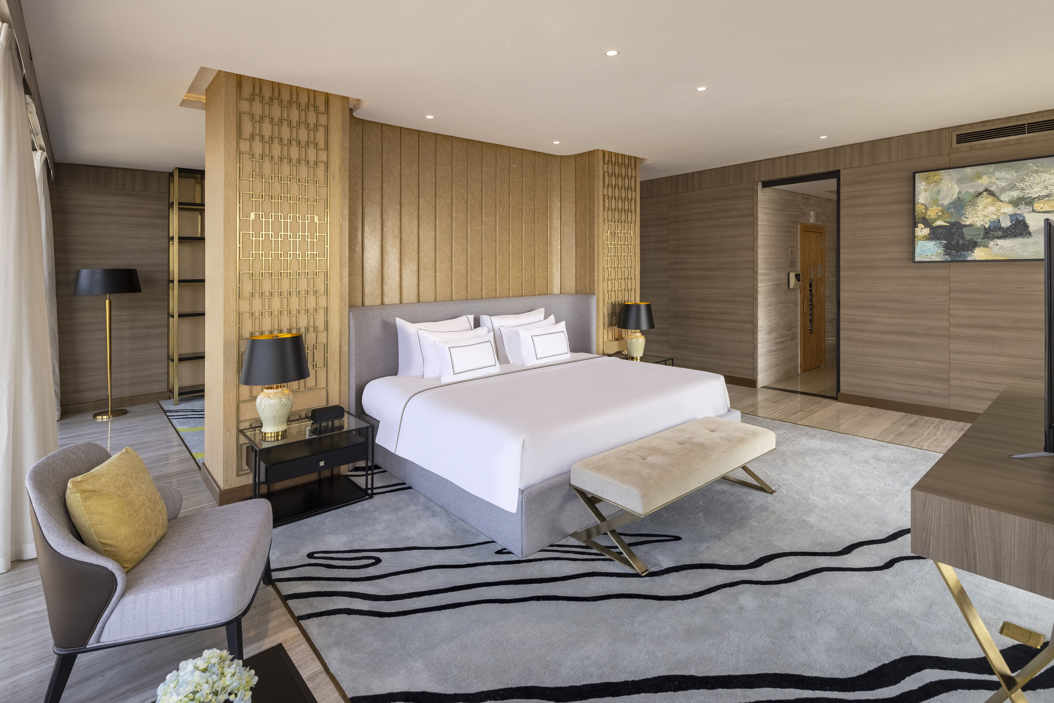 Luxury hotel bedroom with king bed, gold accents, elegant rug, and modern decor.