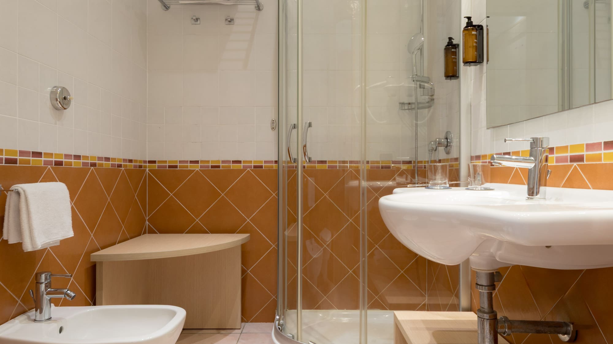 Bathroom with glass shower, sink, toilet, bidet, and terracotta tiled walls.