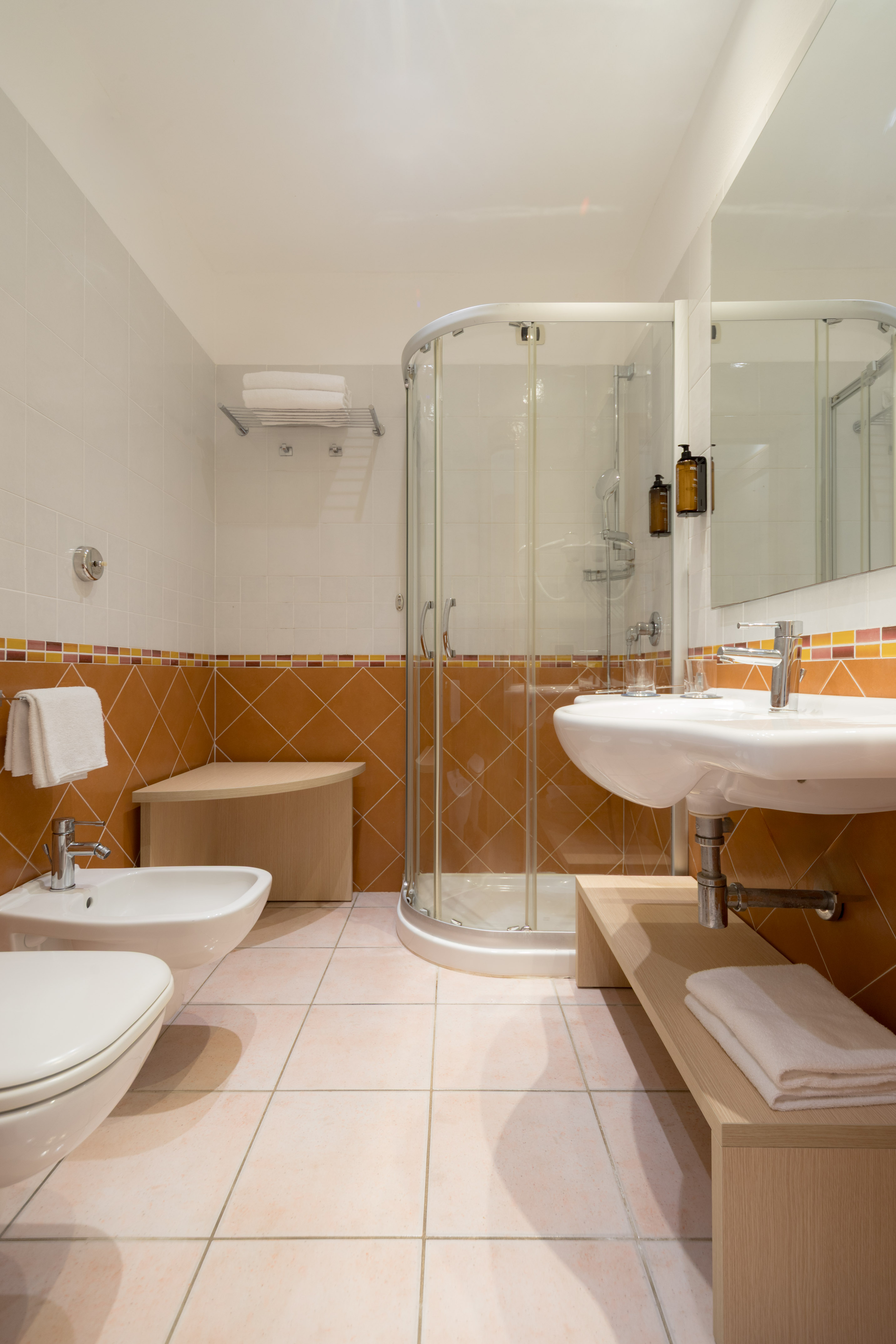 Bathroom with glass shower, sink, toilet, bidet, and terracotta tiled walls.