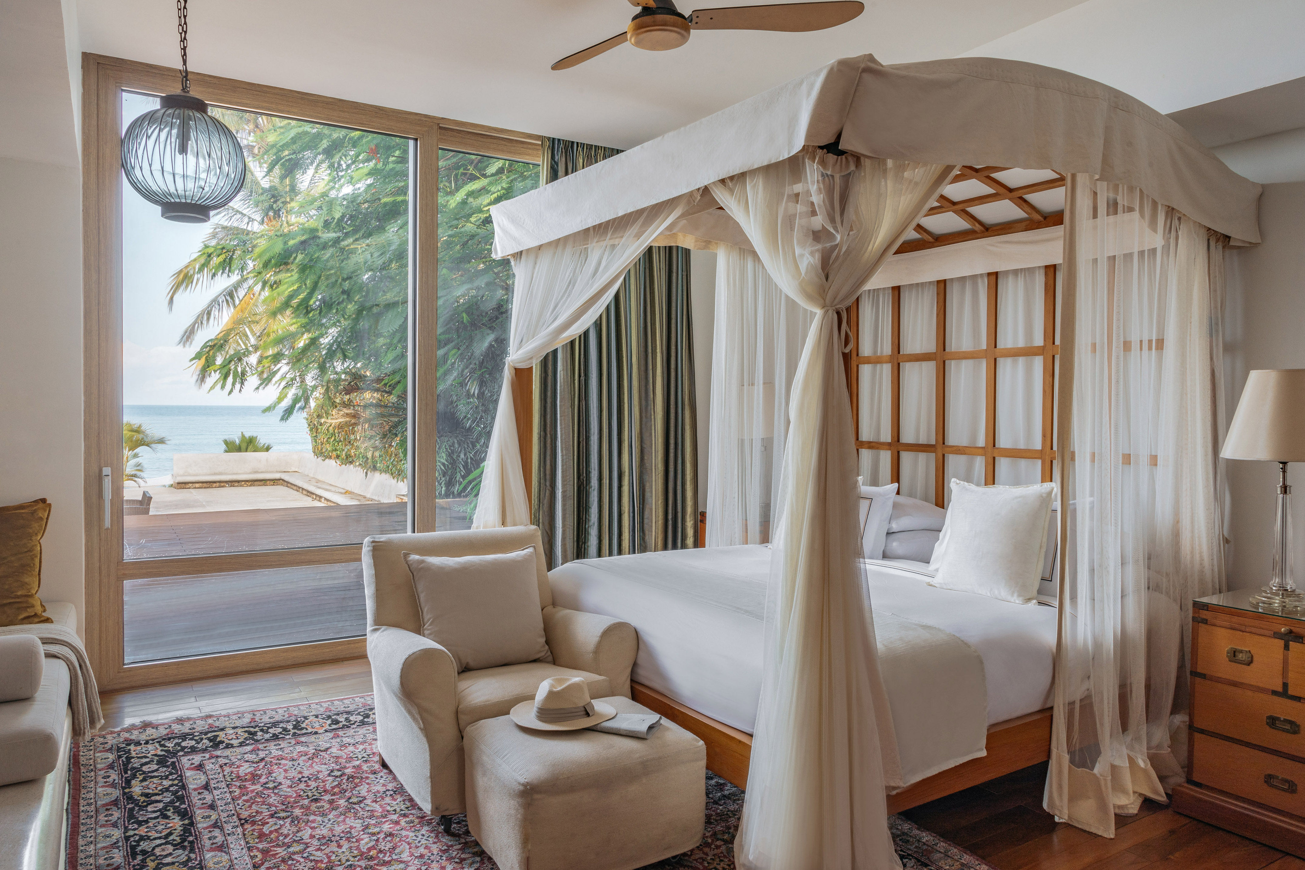 Luxury bedroom with ocean view, four-poster bed, and lush tropical palms.