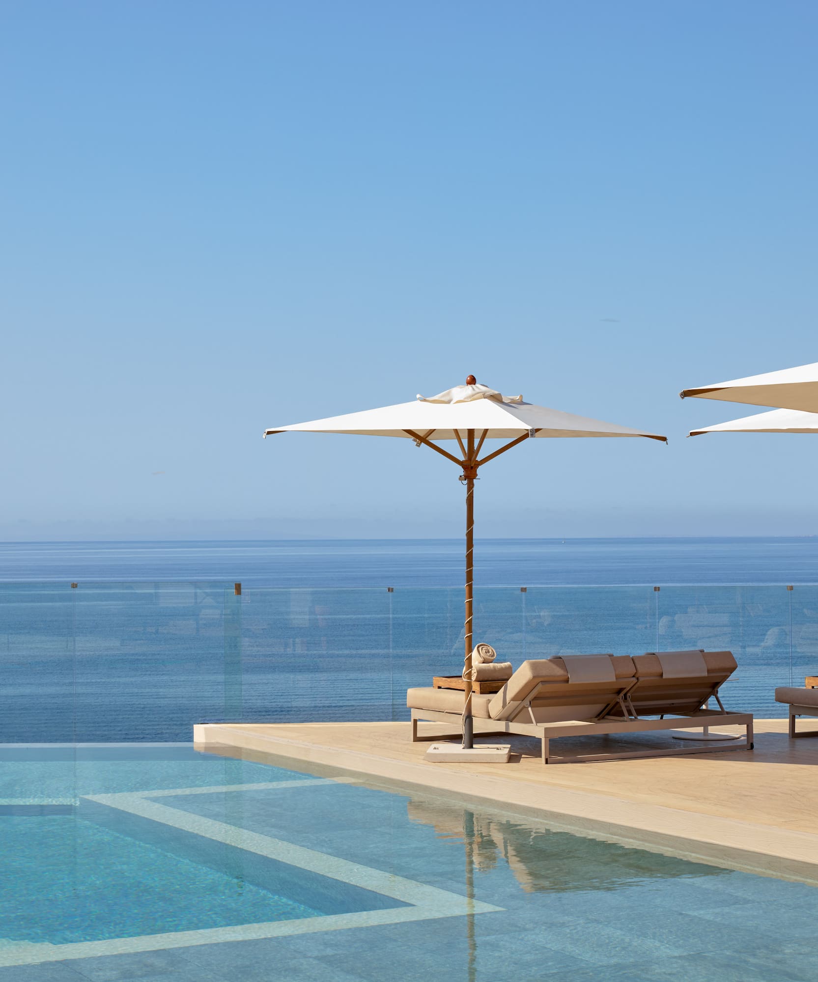 Luxury resort infinity pool with ocean view, sun loungers, and umbrellas.