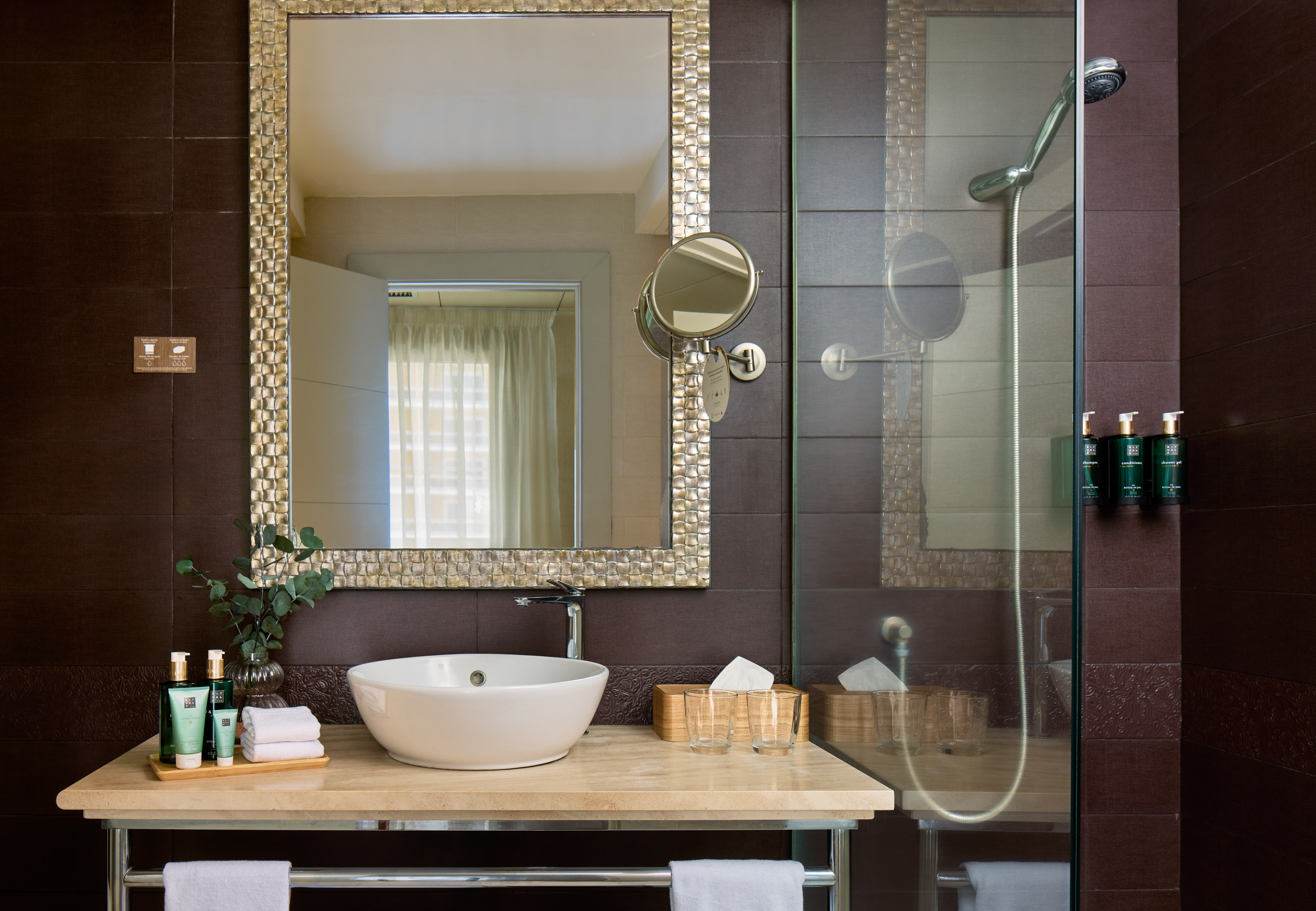 Modern hotel bathroom with vessel sink, decorative mirror, and glass shower.