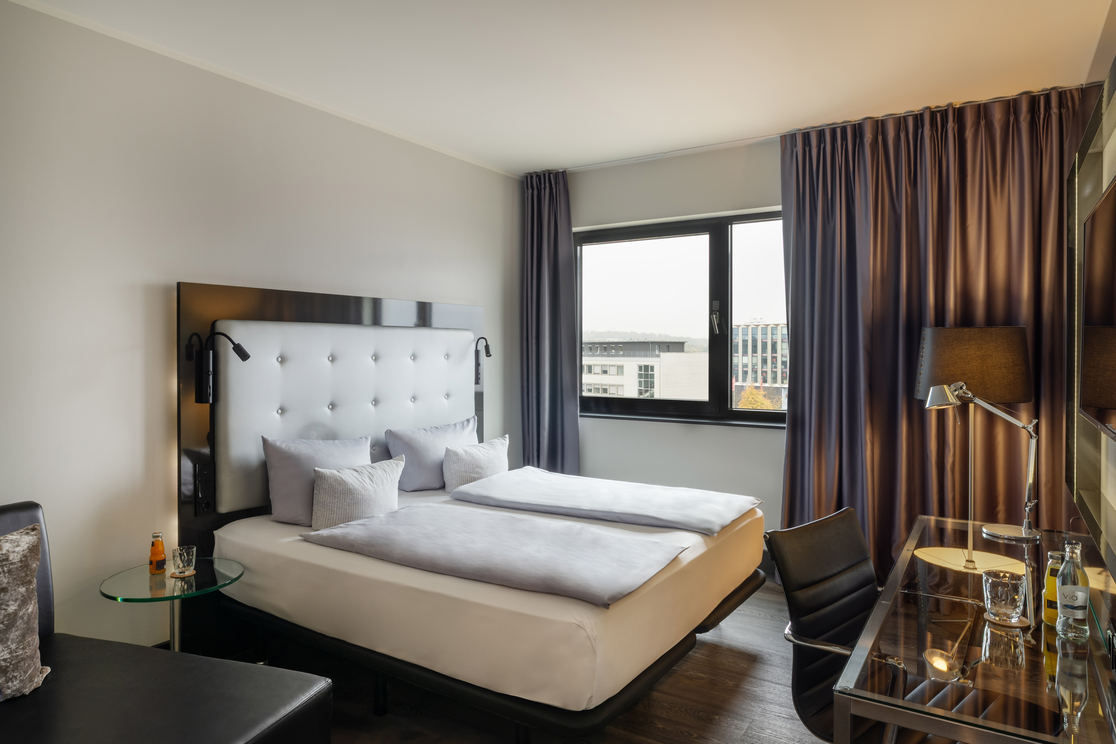 Hotel guest room with modern double bed, padded headboard, and desk.
